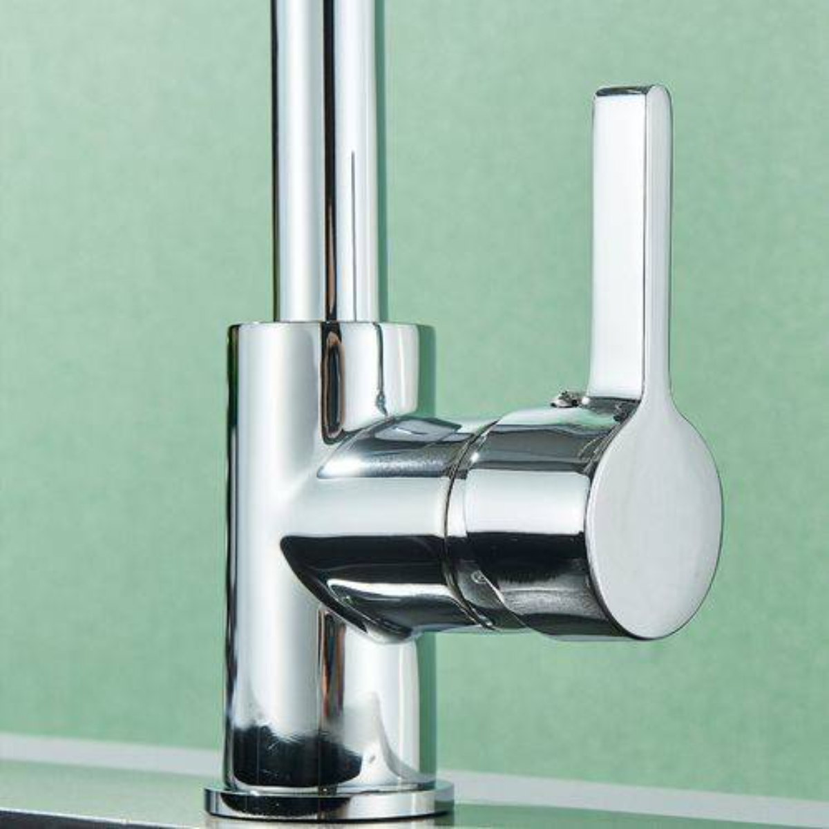 Chromarmatur mit Hebelgriff vor grüner Wand. Die Armatur ist glänzend und reflektierend.