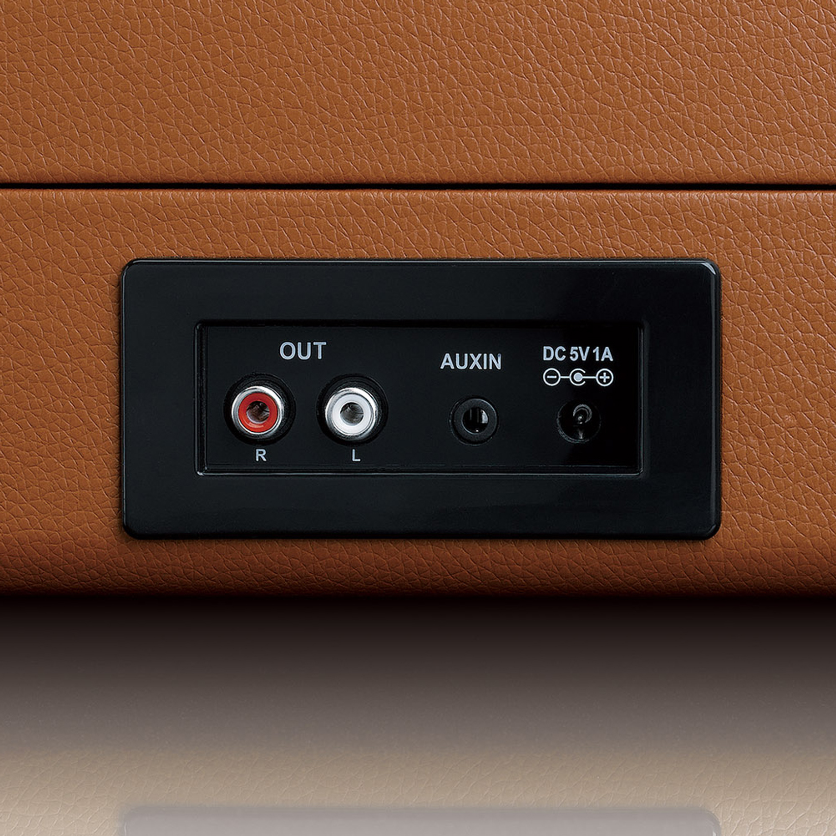 Zbliżenie brązowej skórzanej powierzchni z czarnym panelem zawierającym porty wyjściowe audio.
