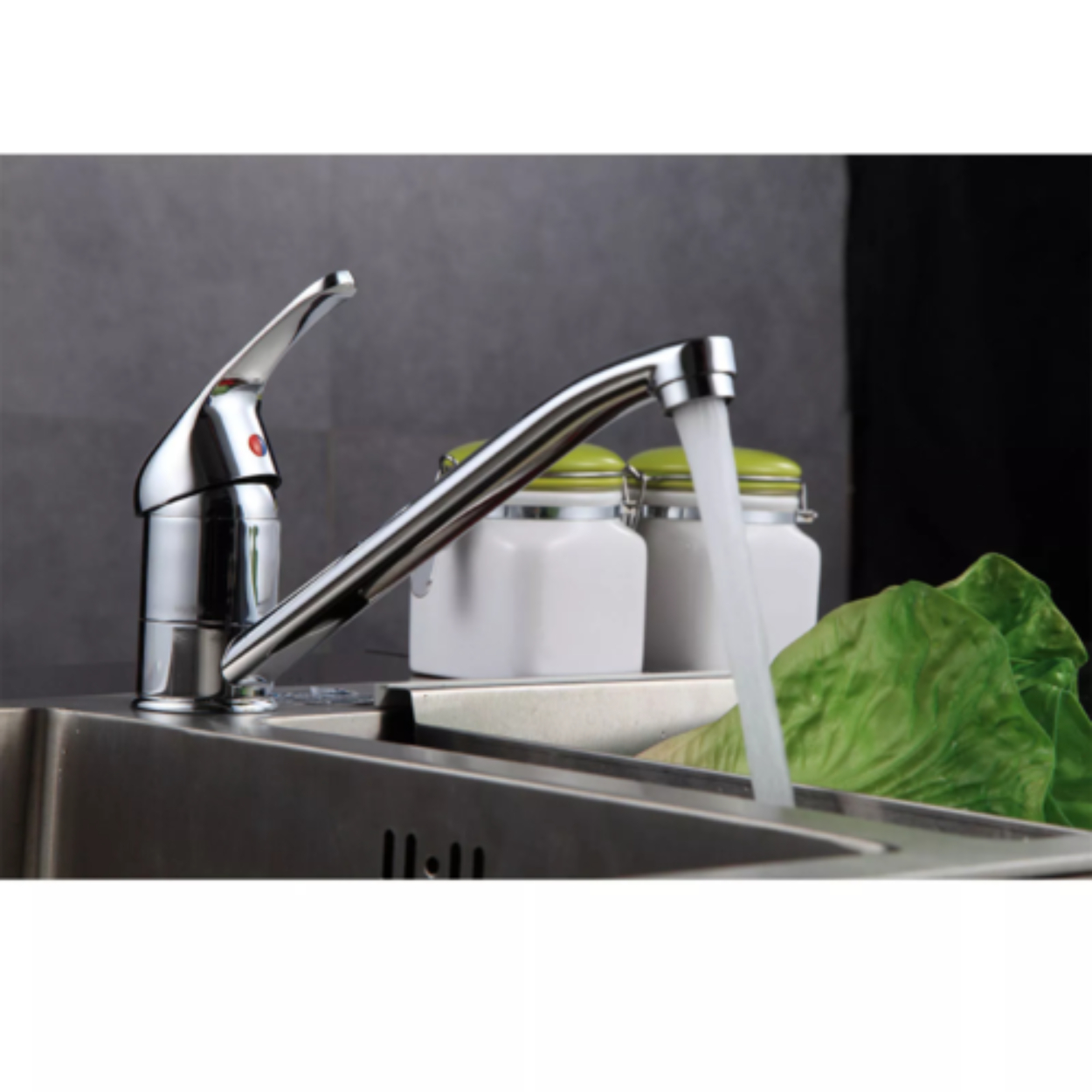 Chrom-Wasserhahn mit Wasser in ein Waschbecken. Gläser und Salat im Hintergrund.