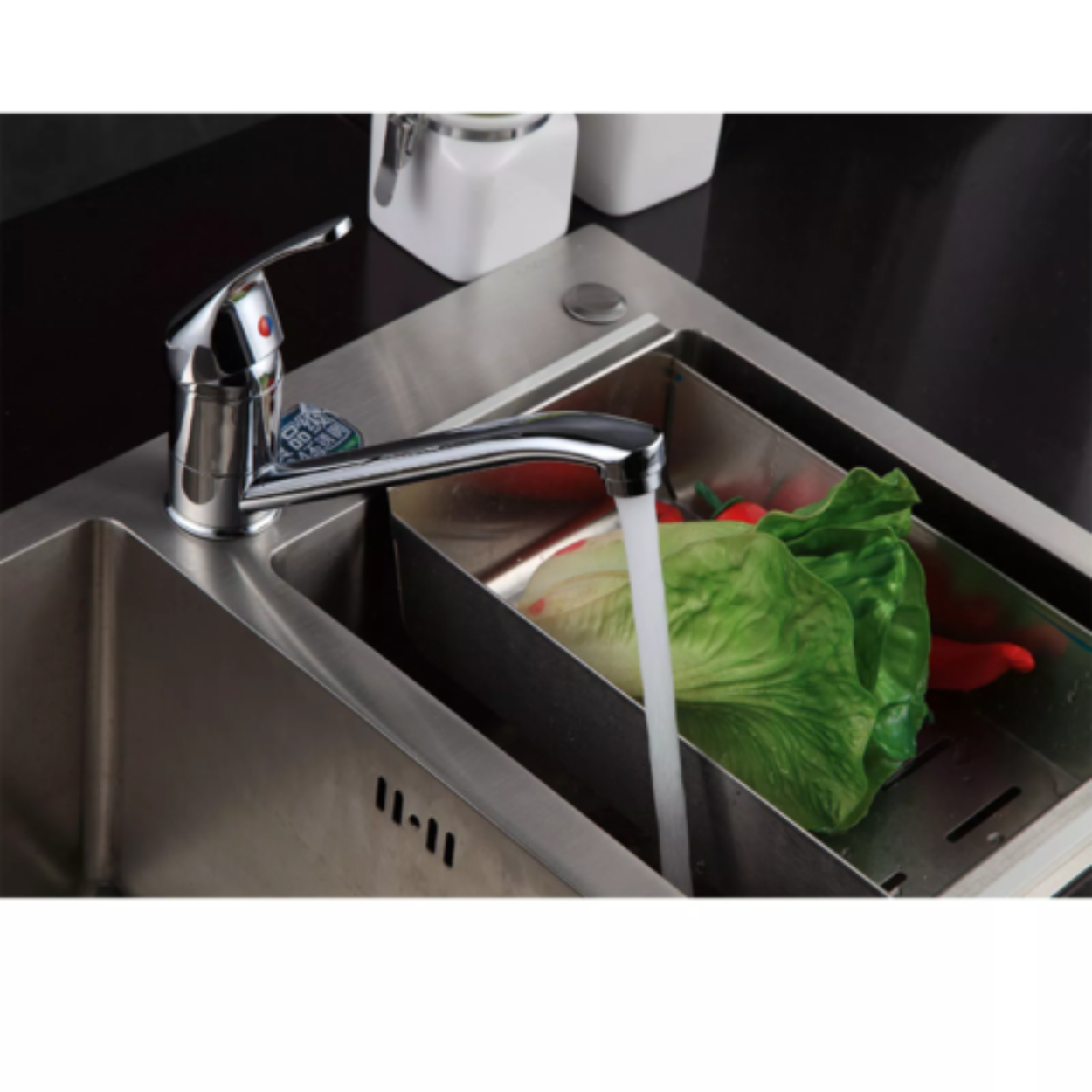 Ein verchromter Wasserhahn mit Wasser, das in ein Edelstahlbecken fließt. Salat und rote Paprika liegen darin.