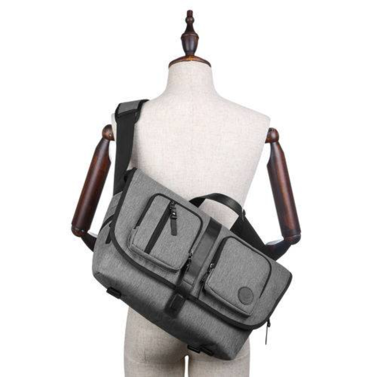 Graue Umhängetasche an einer Schaufensterpuppe. Es hat zwei Vordertaschen und einen schwarzen Riemen.