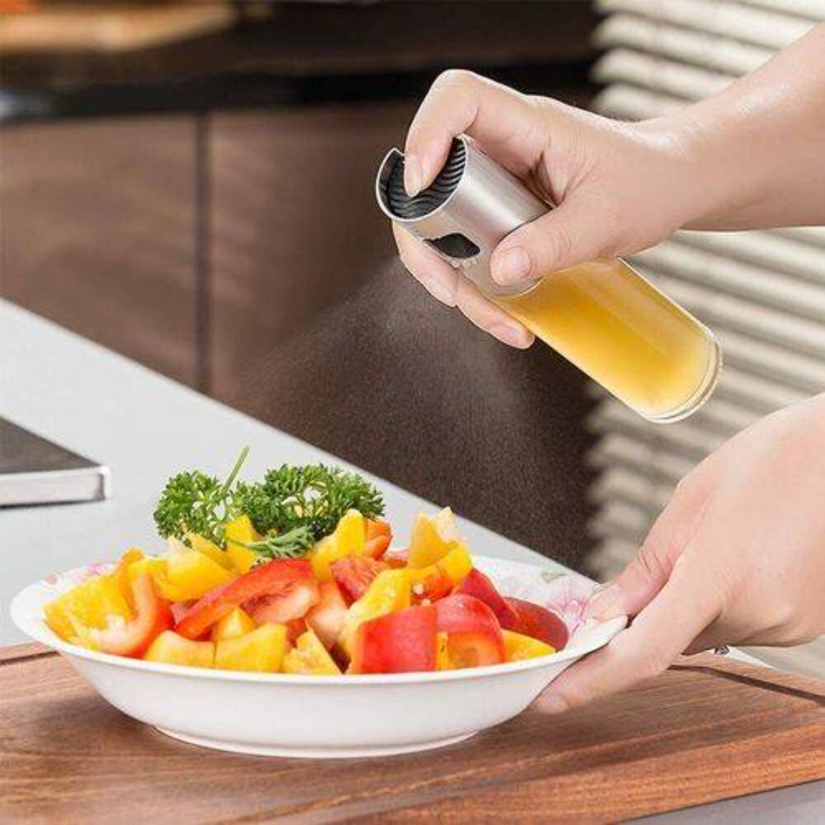 Hand sprüht Öl auf eine Schüssel Salat mit Tomaten und Paprika. Küchenarbeitsplatte im Hintergrund.