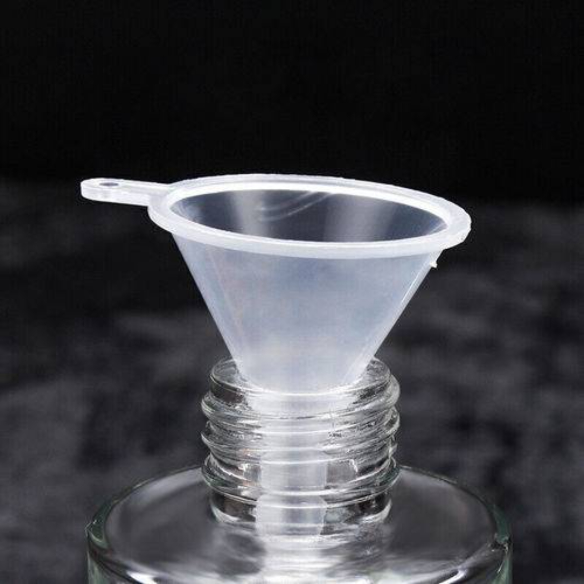 Transparenter Kunststofftrichter im Hals einer Glasflasche, auf dunklem Hintergrund.