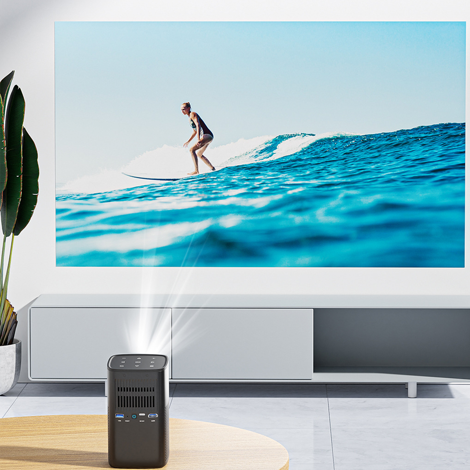 Ein Projektor auf einem Tisch, der einen Surfer auf einer Welle auf eine weiße Wand projiziert. Blauer Himmel.