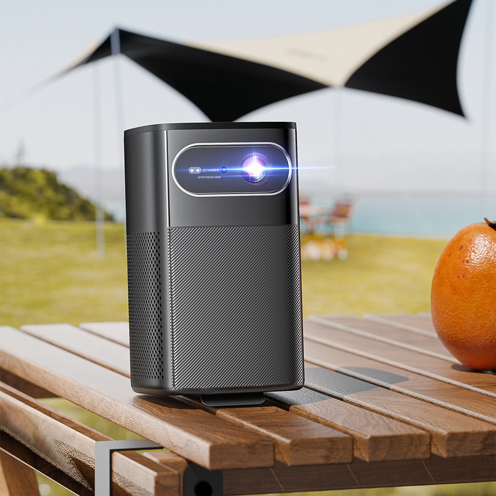 Schwarzer Projektor mit fokussiertem Licht auf einem Holztisch, orangefarbene Frucht und Strandzelt.