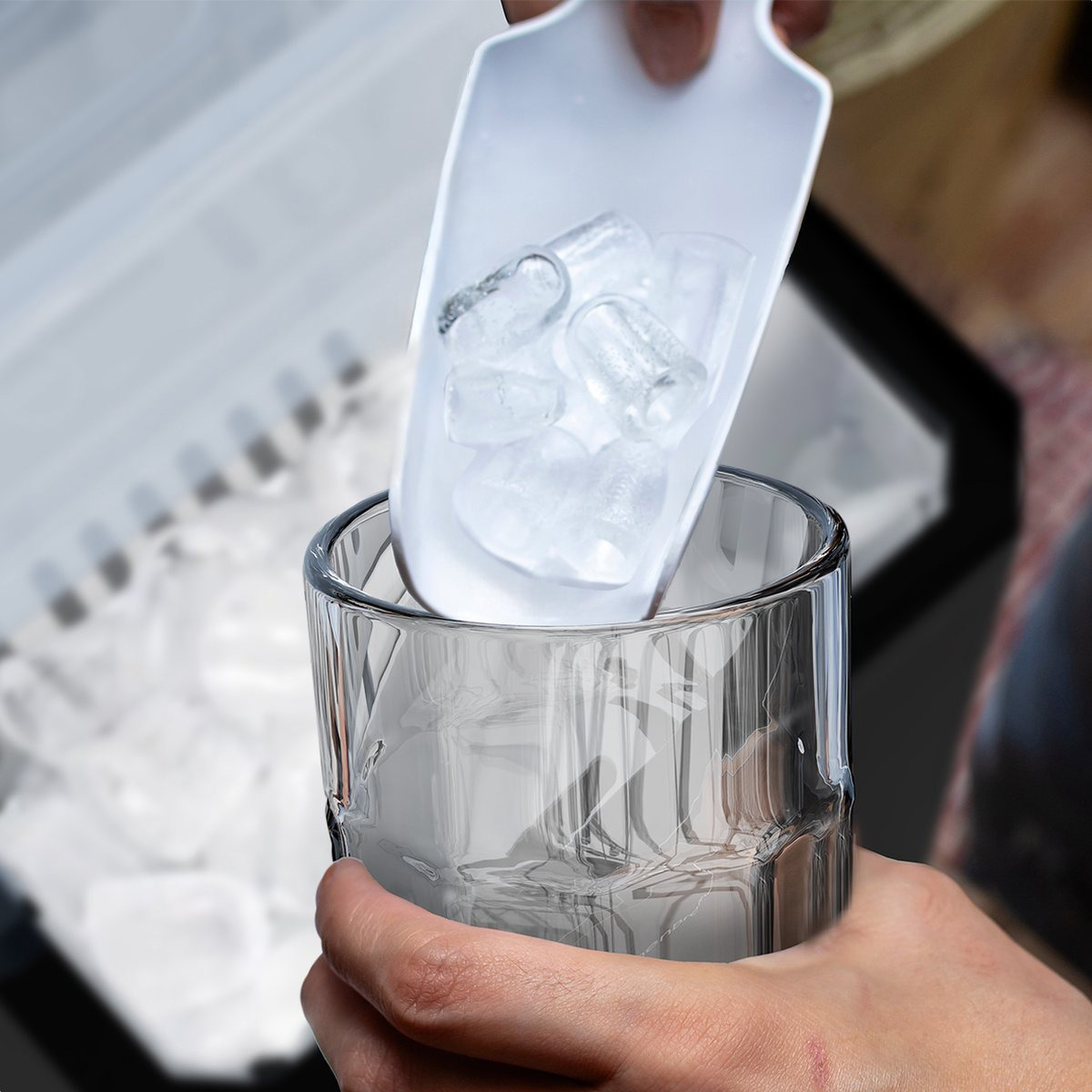 Person putting ice cubes into a glass. The glass is near a container of ice.