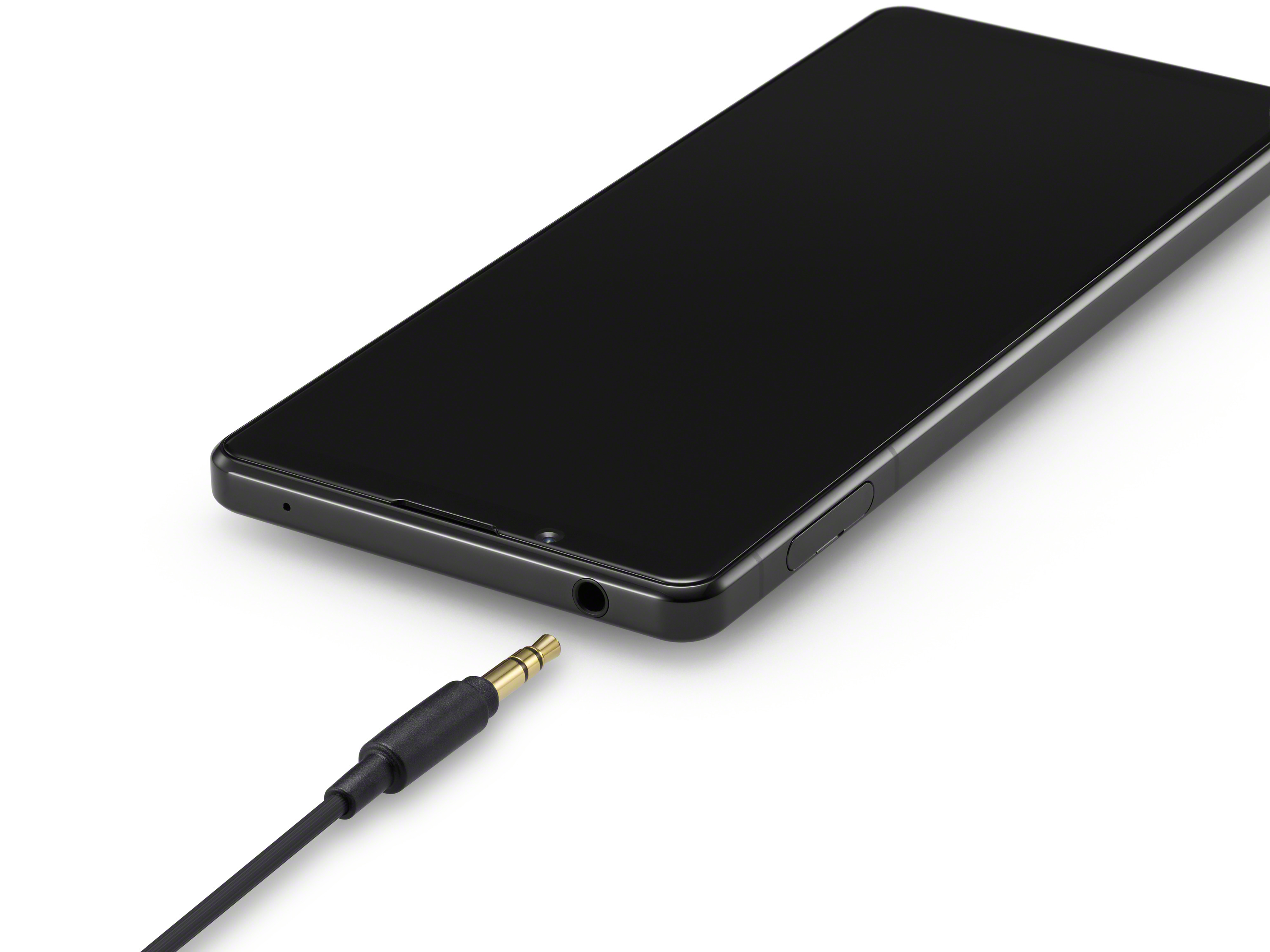 Ein schwarzes Smartphone mit Kopfhöreranschluss, ein Kabel ist angeschlossen. Das Telefon liegt auf weißem Untergrund.