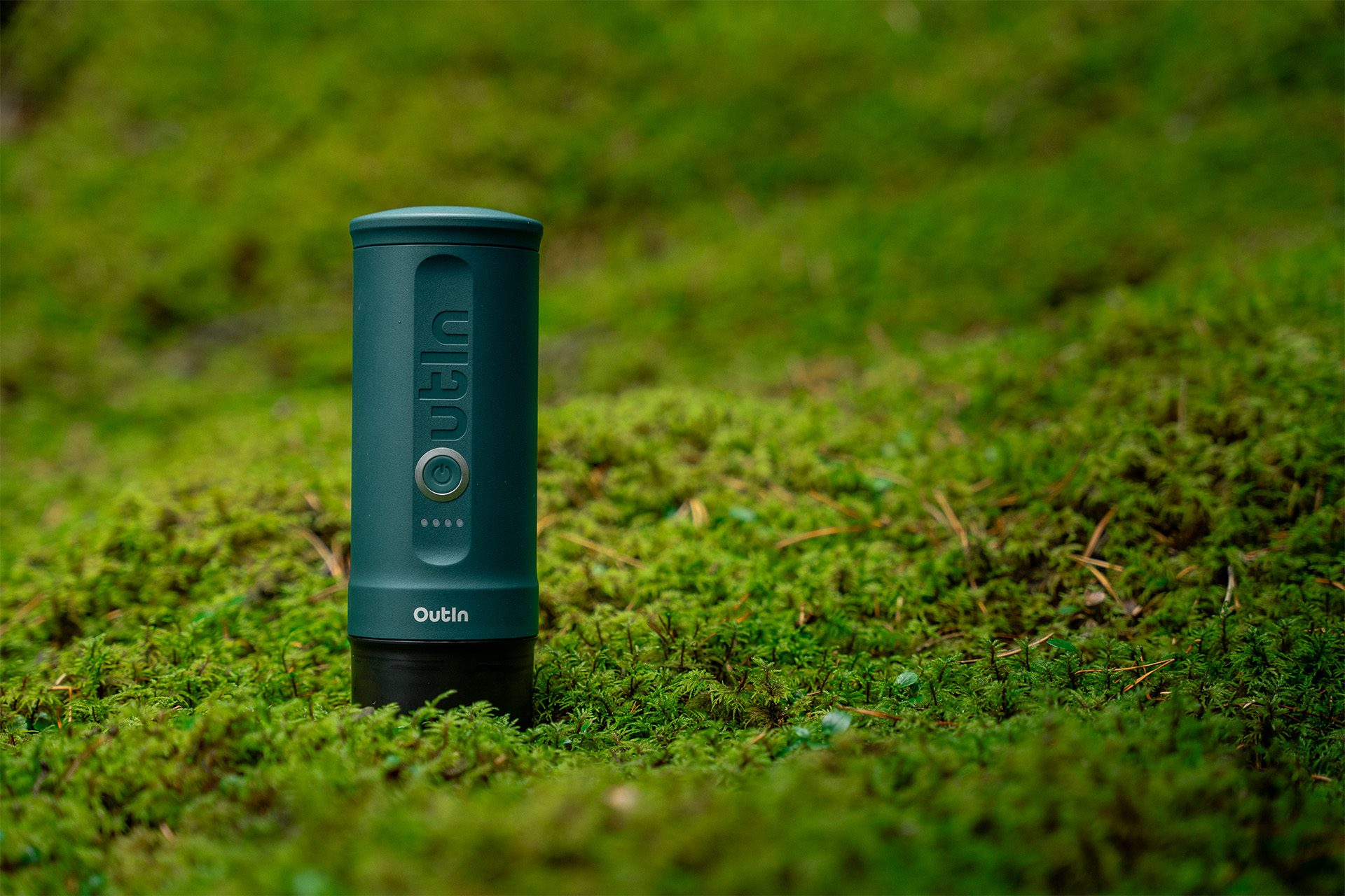 Groen cilindrisch object met een aan/uit-knop op een mosachtige achtergrond, met Outln.