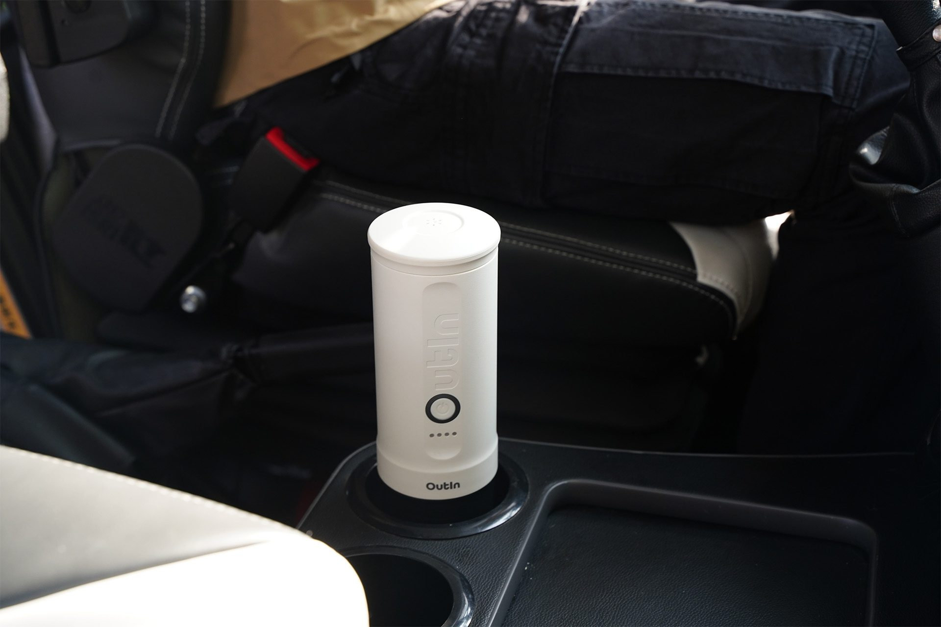 Draagbare espressomachine in de bekerhouder van een auto. Outin merk. Wit en zwart met een knop.