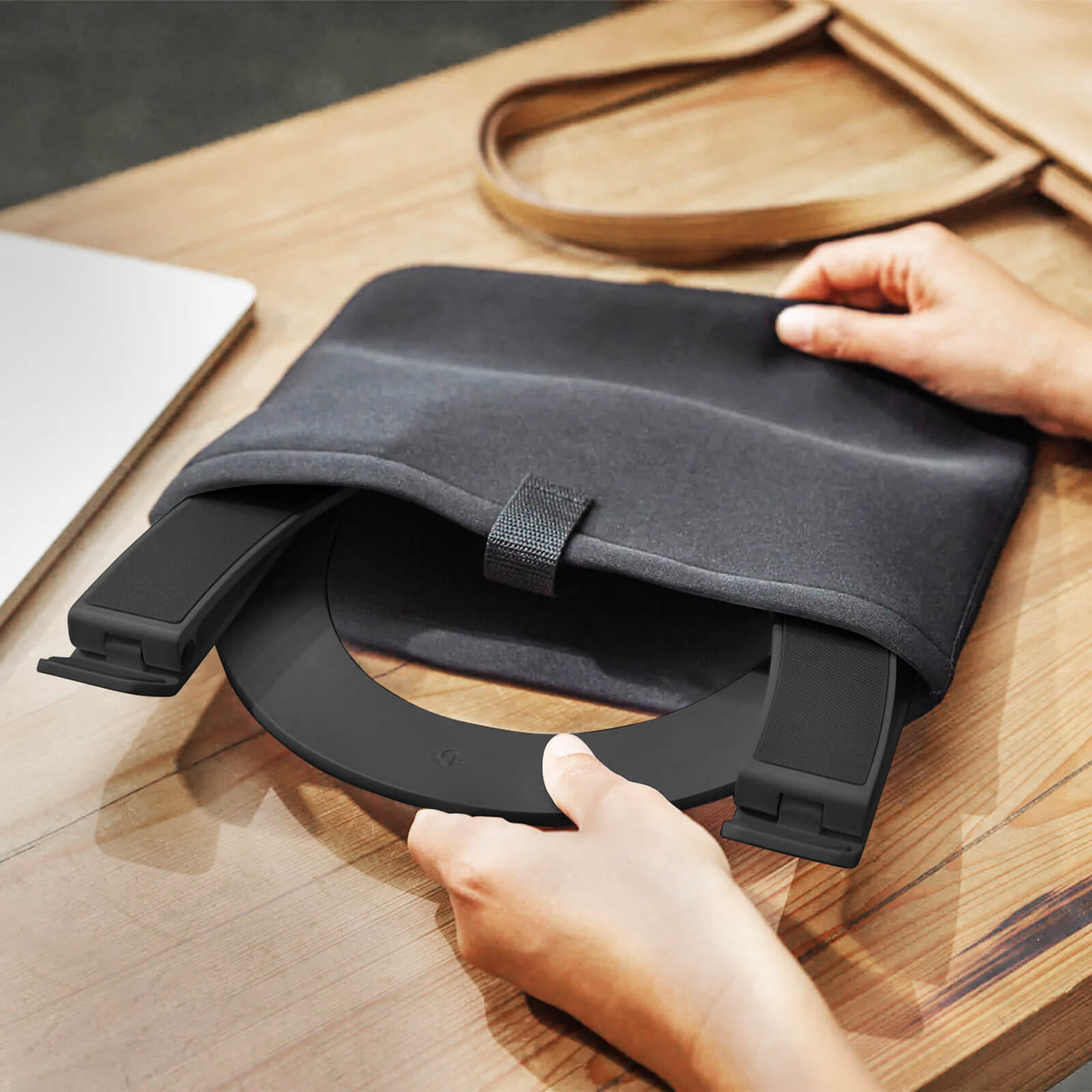 A black laptop stand in a black case. The stand is being taken out of the case. A wooden table.