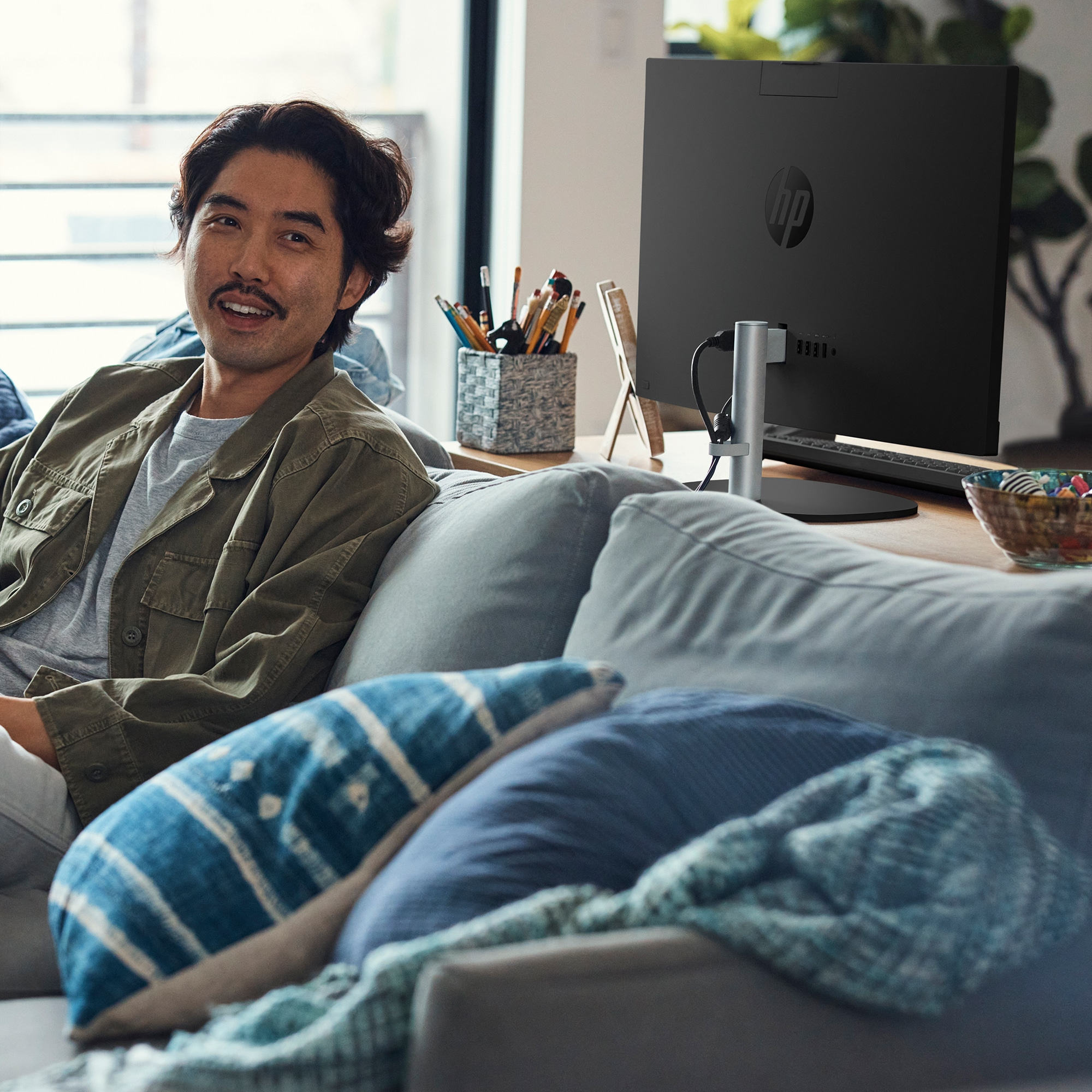 A man is sitting on a couch in front of an HP all-in-one computer.