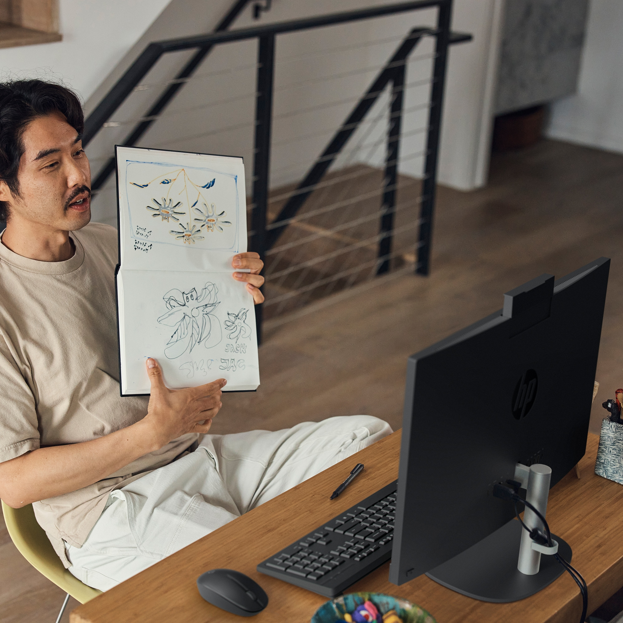 A person holding a drawing, looking at an HP all-in-one computer screen, with keyboard and mouse.