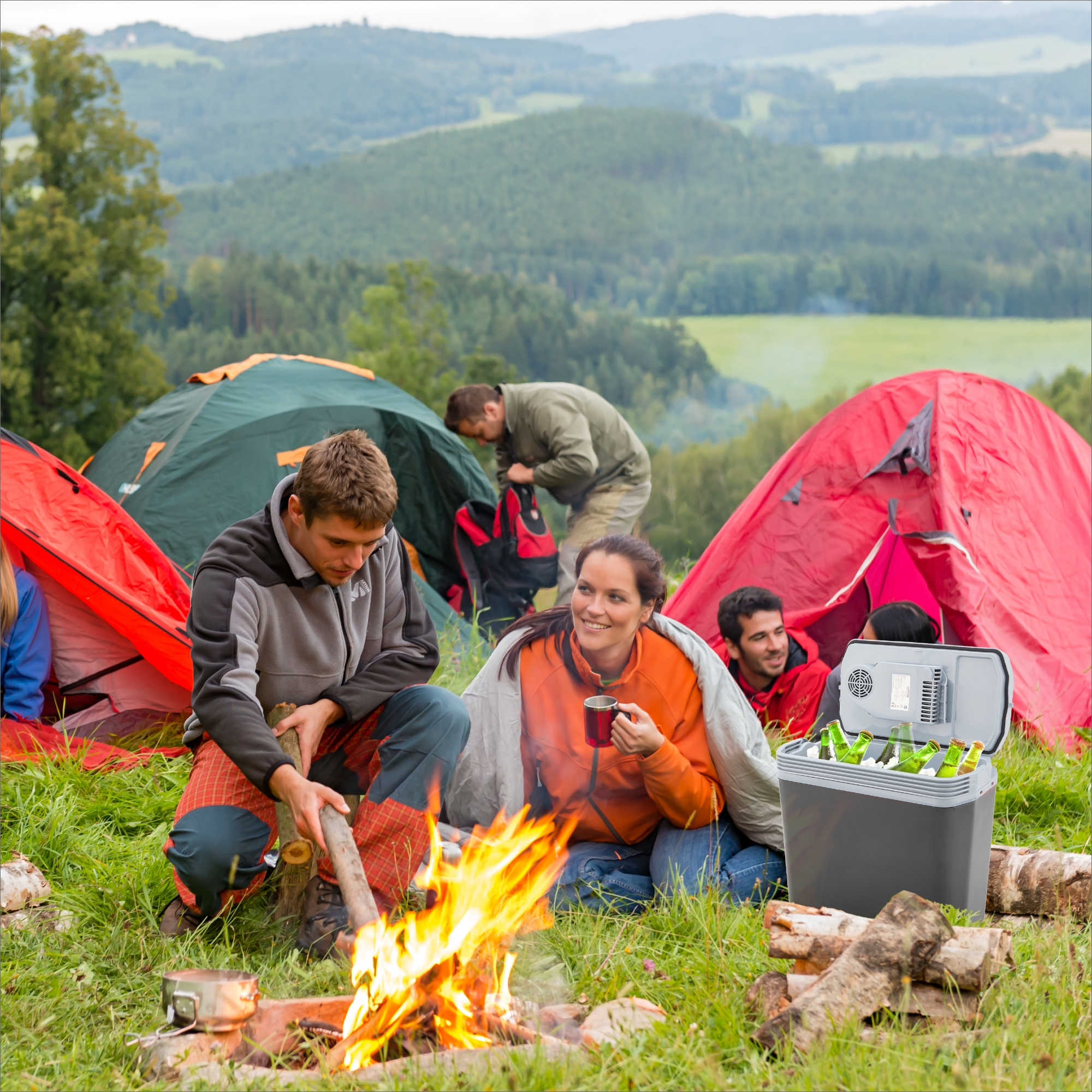 Eine Campingszene mit Zelten, Menschen am Feuer und einer Kühlbox. Grüne Hügel und Himmel im Hintergrund.