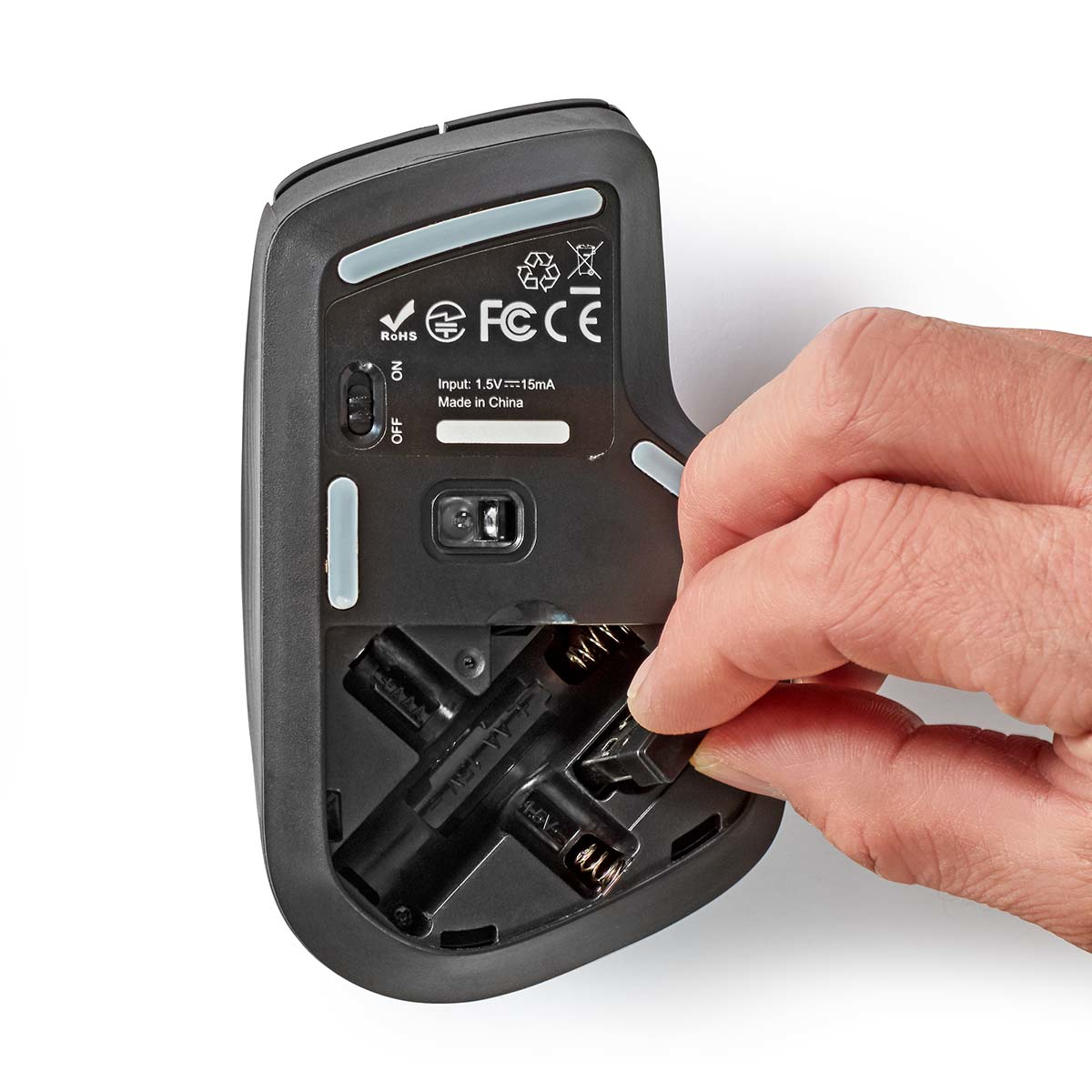 Osoba wkładająca baterie do czarnej myszy bezprzewodowej. Widoczny spód myszy.