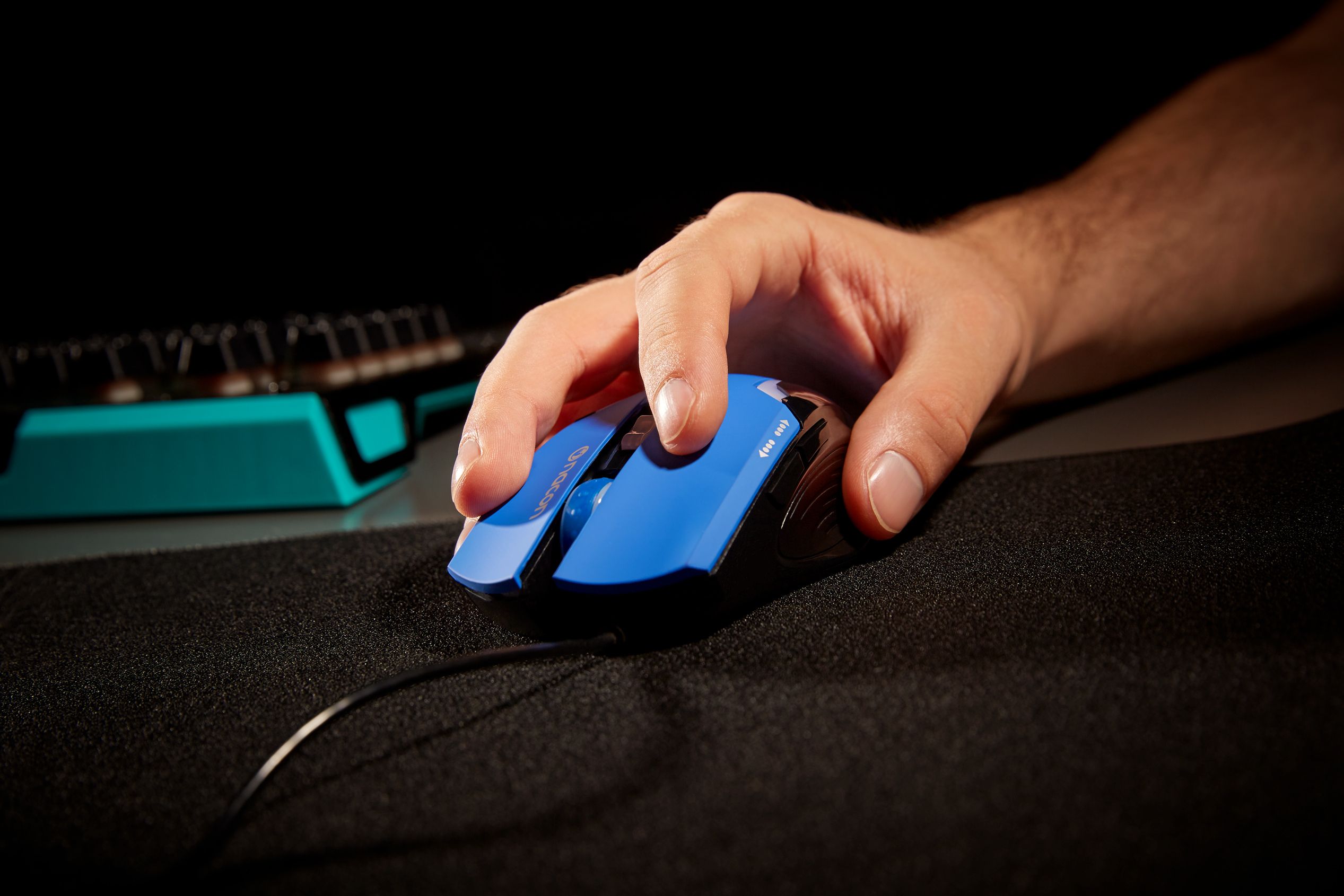 Ręka używająca niebiesko-czarnej myszy gamingowej. Mysz na czarnej podkładce.