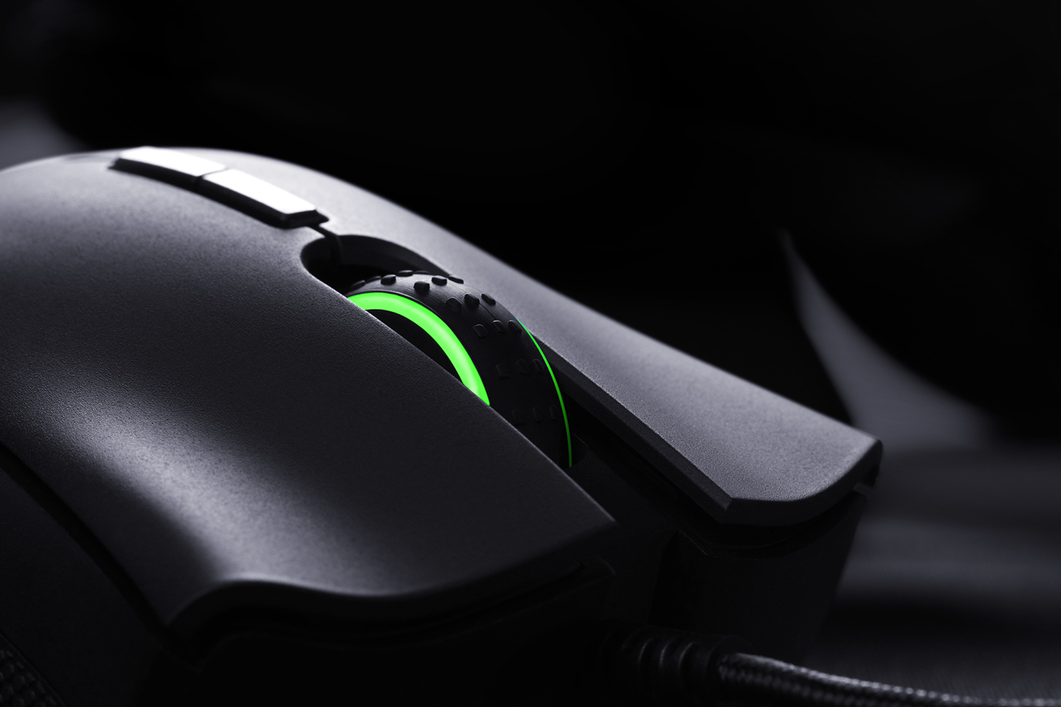 Nahaufnahme einer schwarzen Gaming-Maus mit grün beleuchtetem Scrollrad auf dunkler Oberfläche.