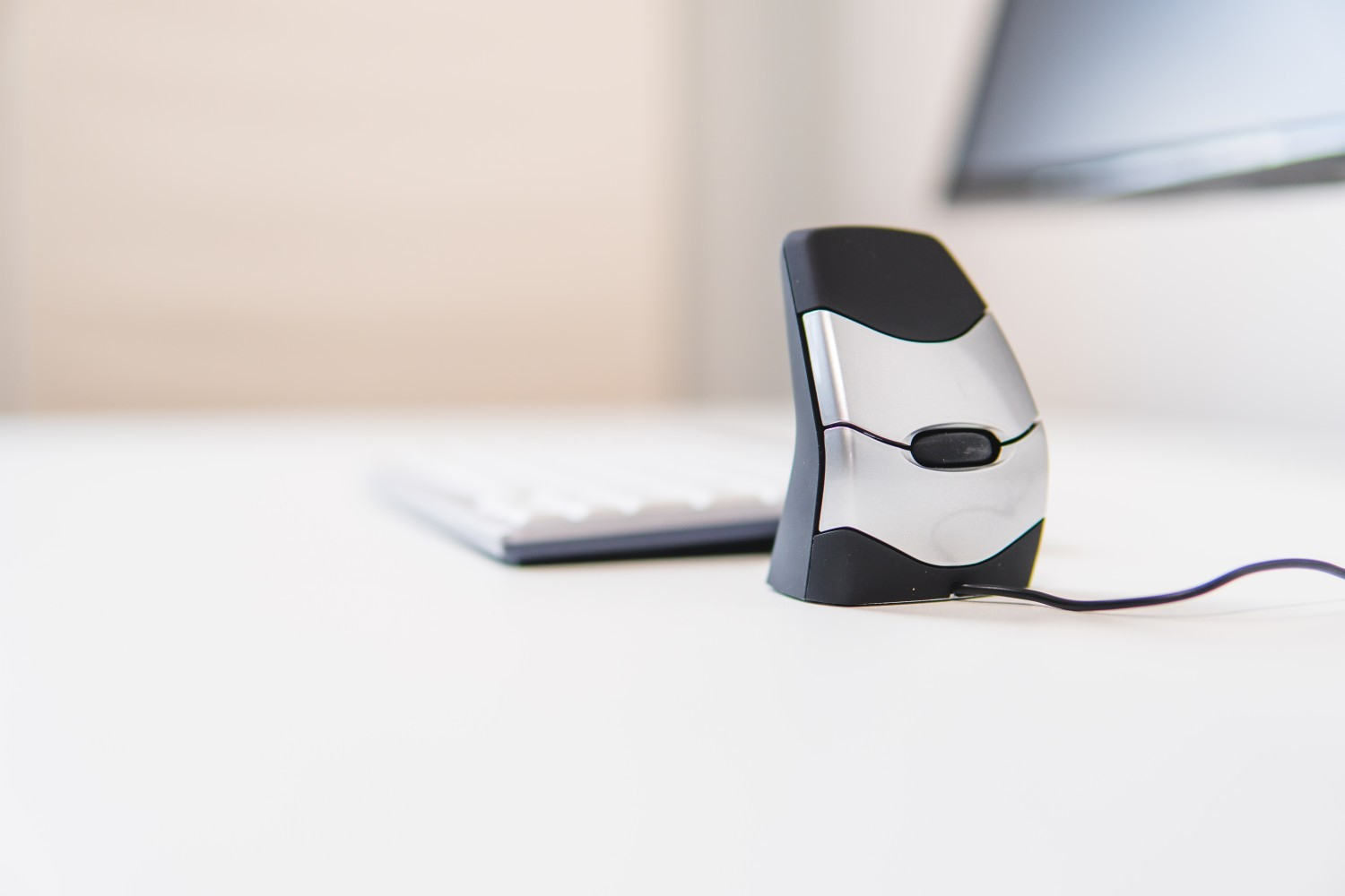 Ergonomic mouse and keyboard on a white desk. Black mouse, silver and black keyboard.