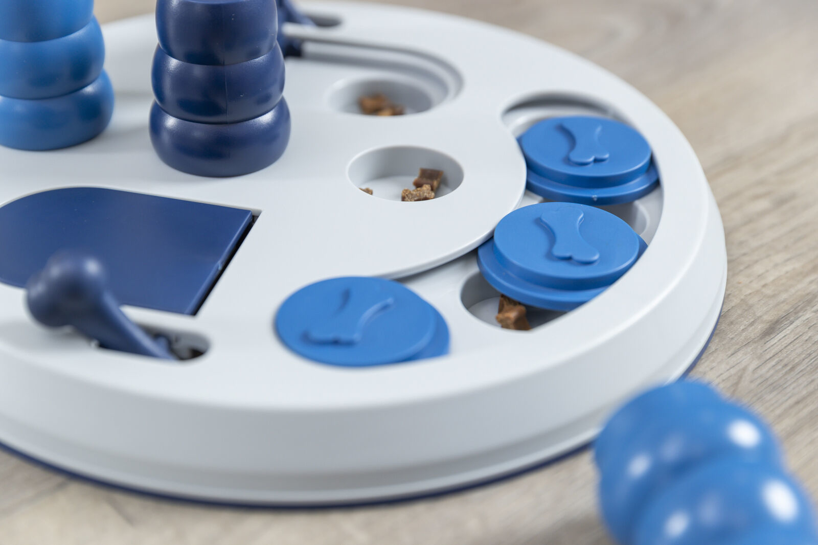 Zabawka logiczna dla psa w kolorze białym i niebieskim, z widocznymi kawałkami jedzenia w otworach.