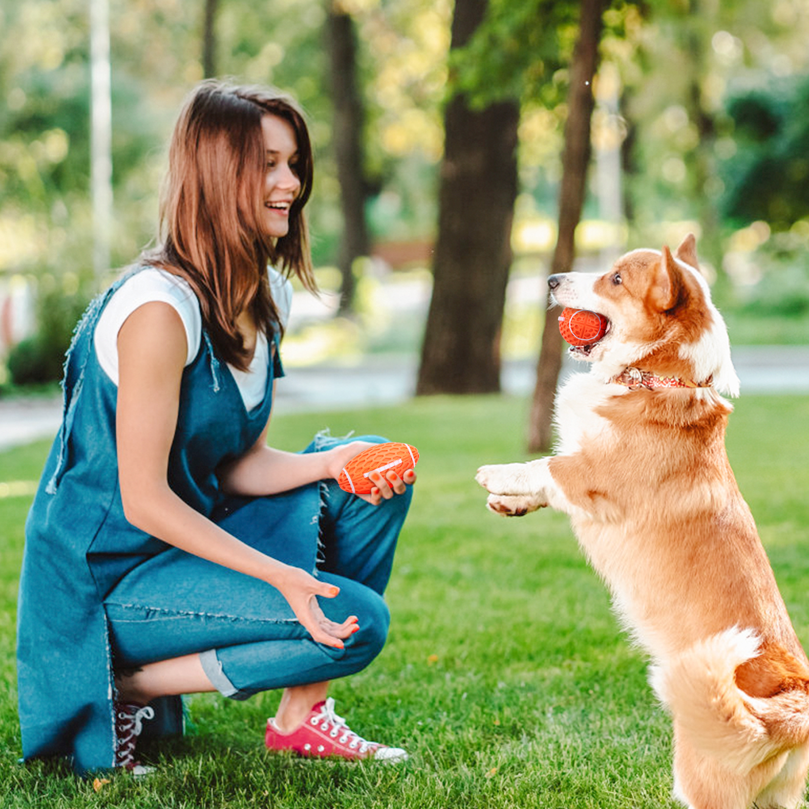 Mujer con vestido de mezclilla jugando con un Corgi en un parque, sosteniendo una pelota naranja.