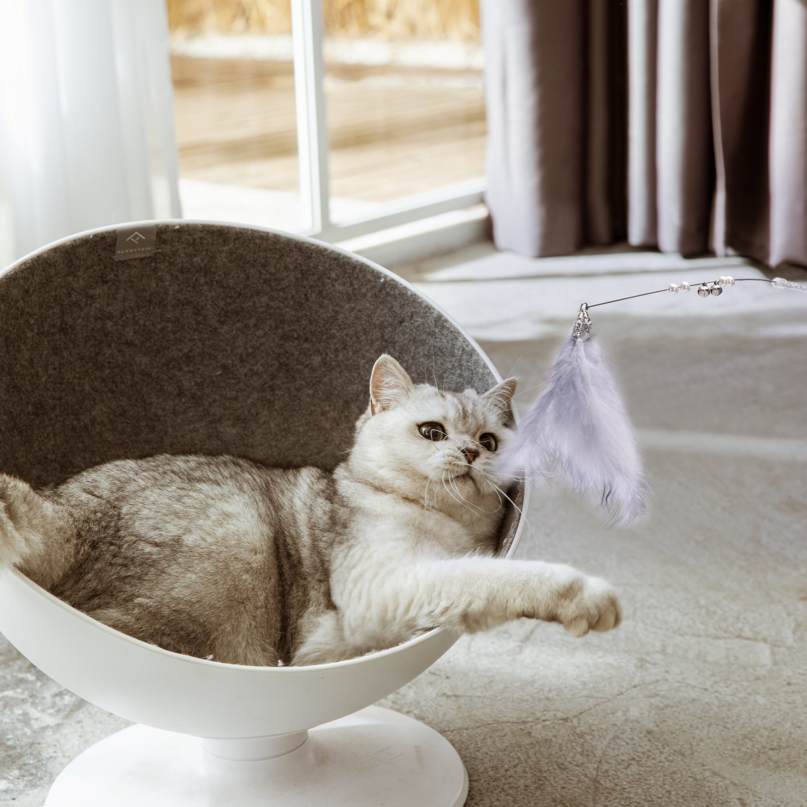 Un gato en una cama para gatos blanca y gris, jugando con un juguete de plumas.