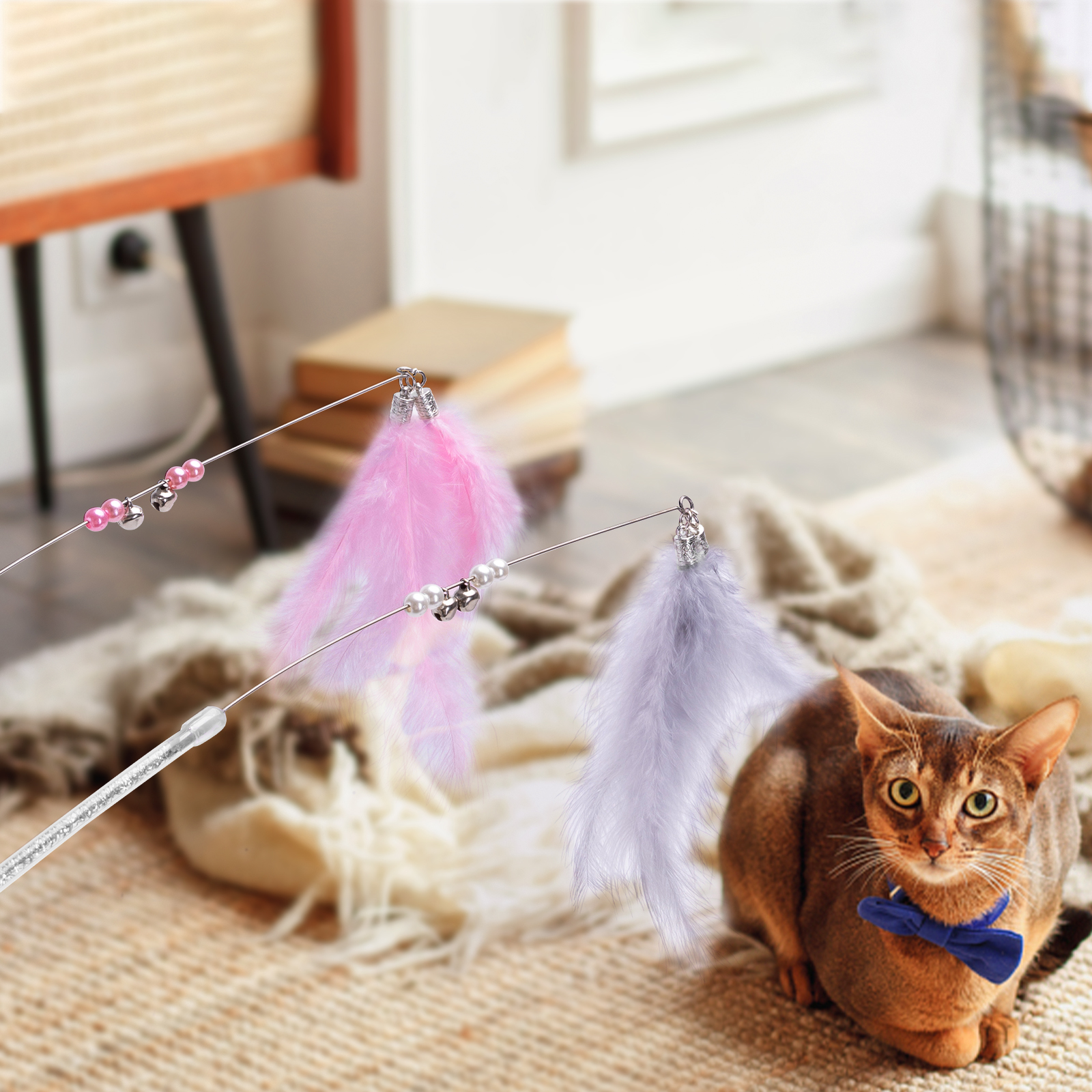 Un gato marrón con pajarita azul jugando con juguetes de plumas colgando de arriba.