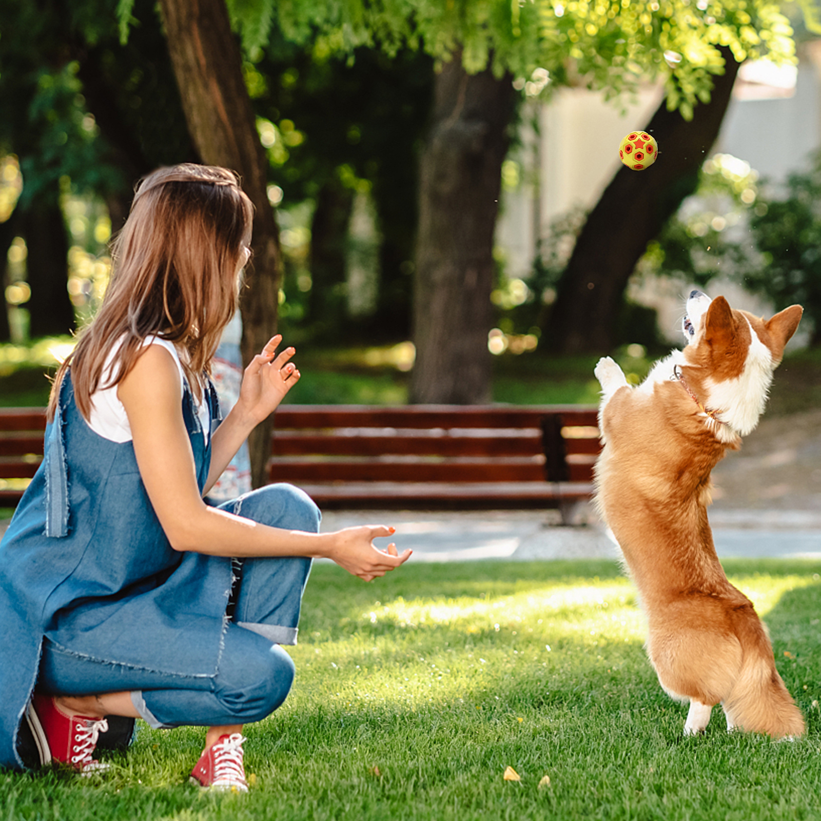 Mujer en mezclilla juega con perro en parque, lanzando pelota.