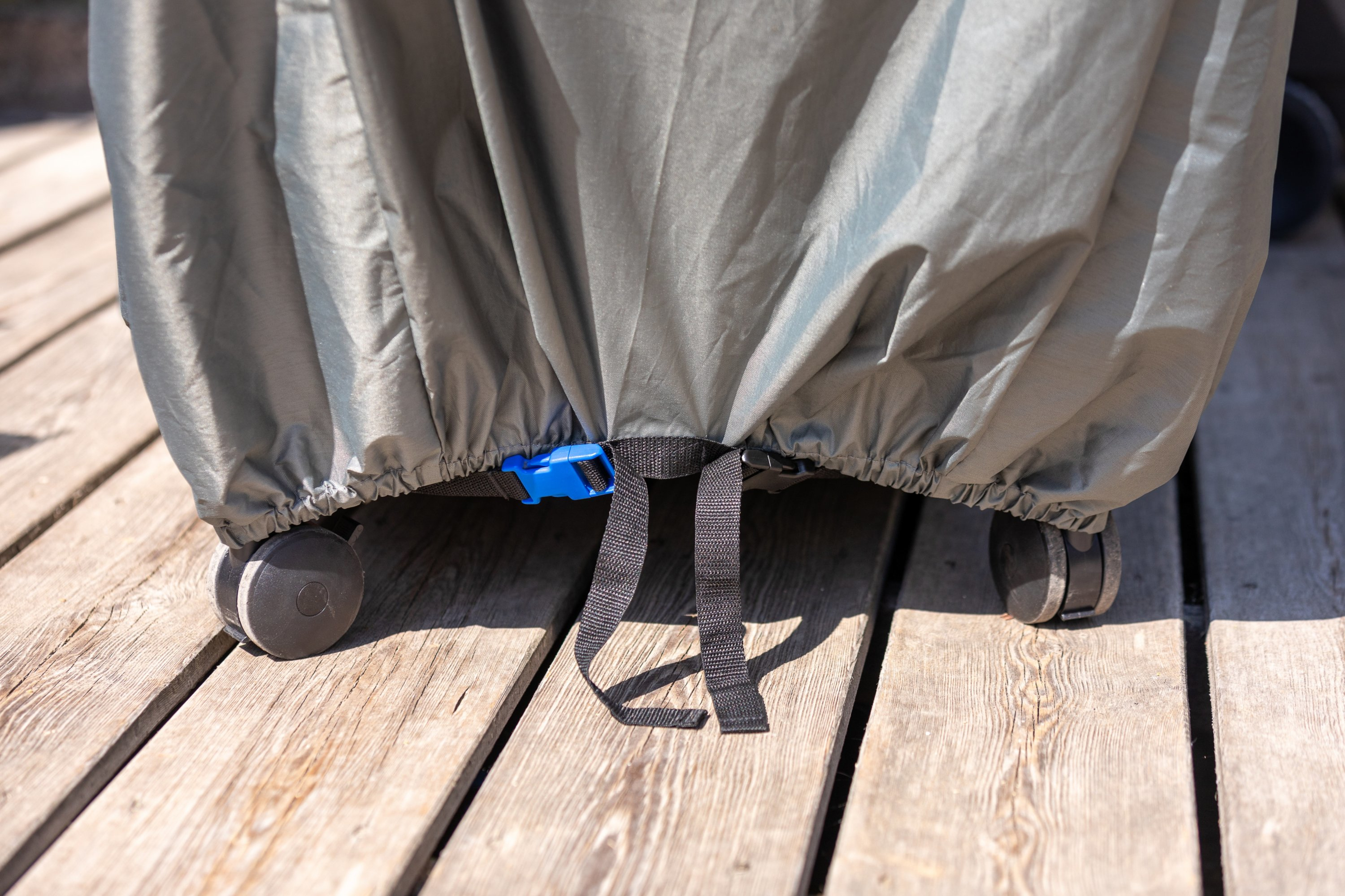 Szara osłona na kołowym obiekcie, zabezpieczona niebieską klamrą i czarnymi paskami, na drewnianej powierzchni.