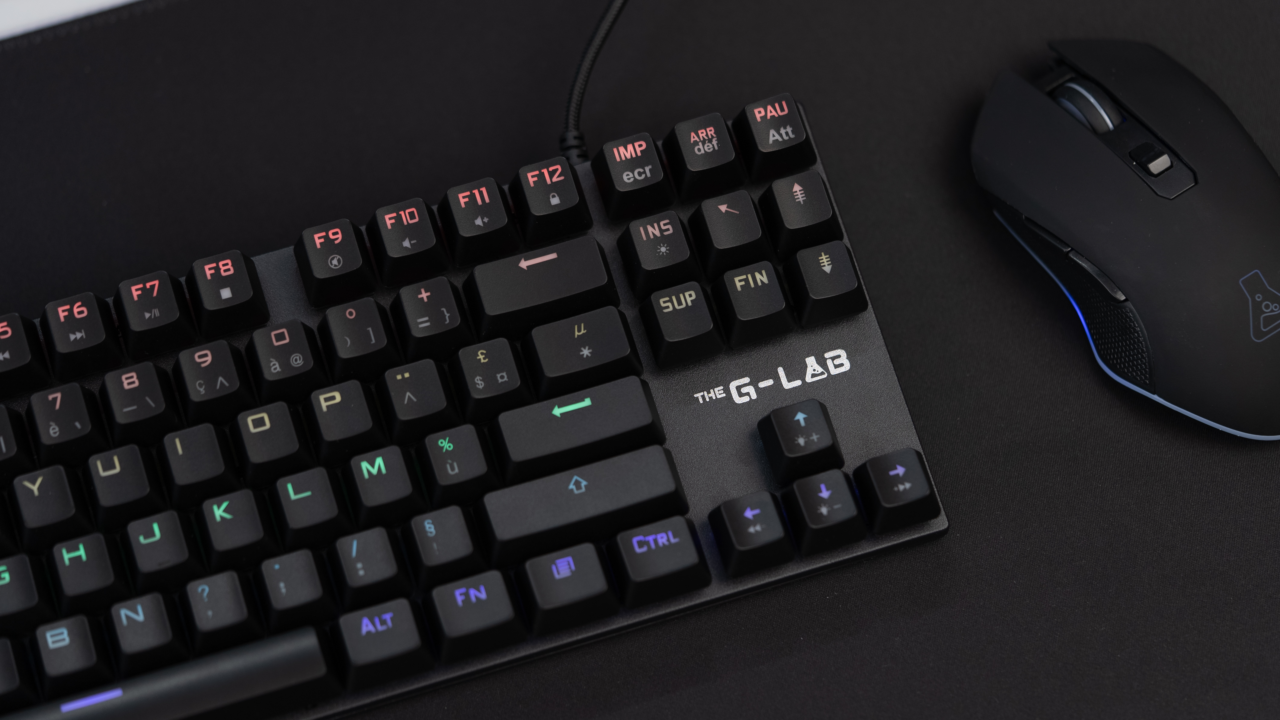 Czarna klawiatura i mysz na ciemnej powierzchni. Klawiatura ma podświetlane klawisze, a mysz logo.