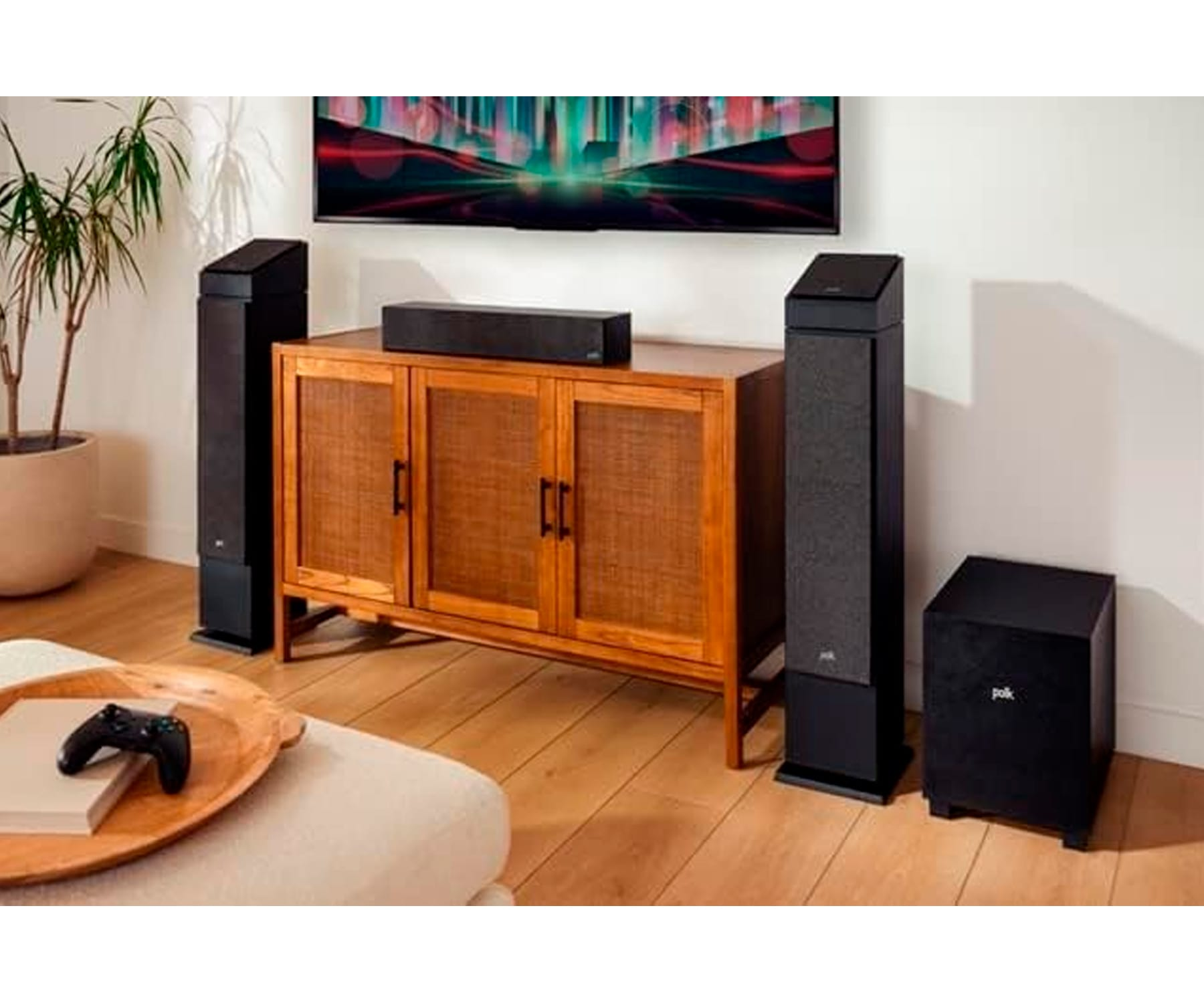 Configuración de entretenimiento en casa con altavoces, TV, mueble y mando de juegos.