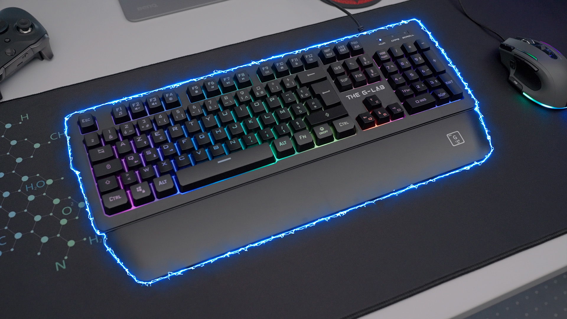 Czarna klawiatura z podświetleniem RGB na podkładce. Mysz i gamepad po lewej.