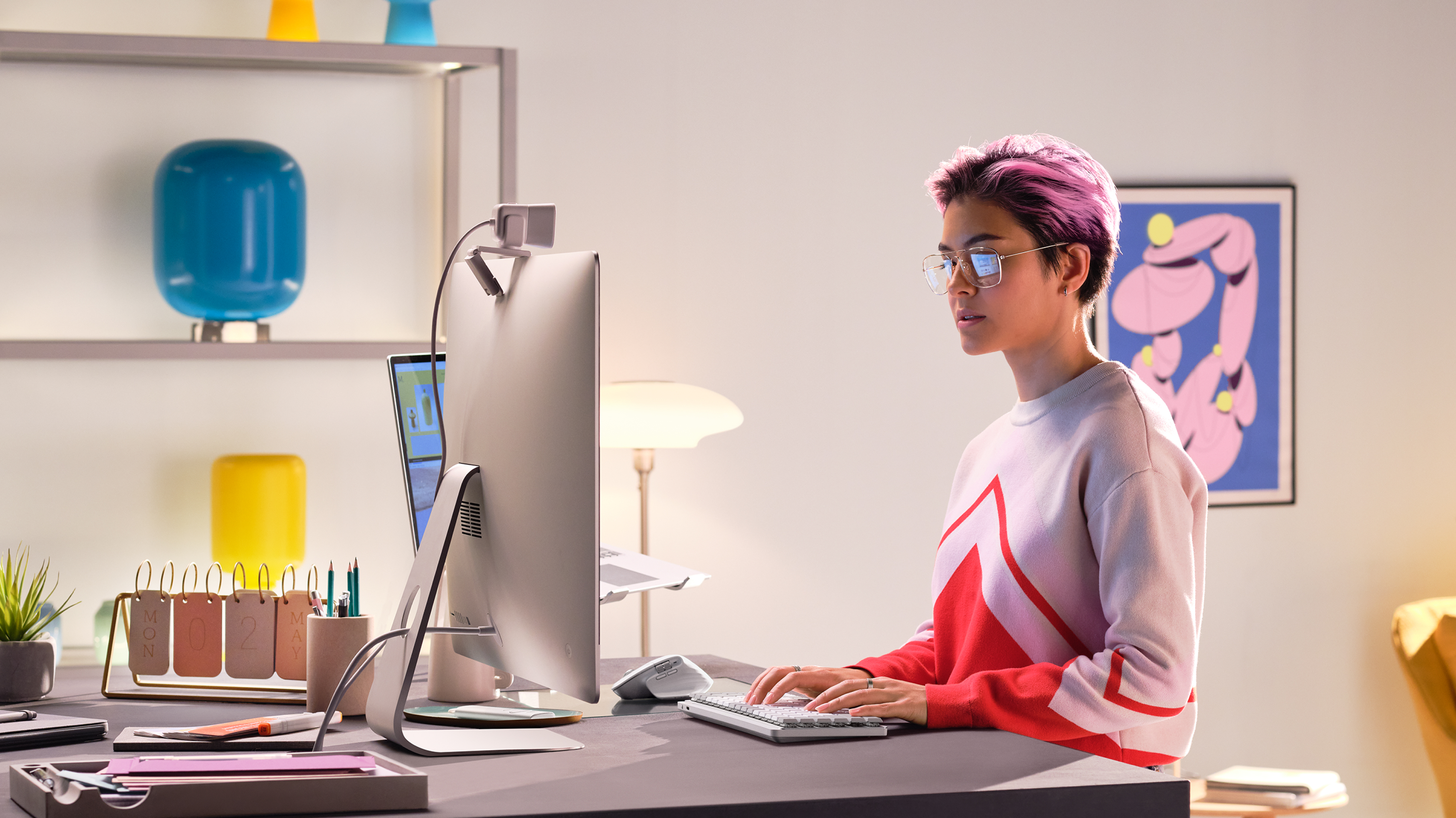 Mujer con pelo rosa trabajando en un escritorio con una computadora.
