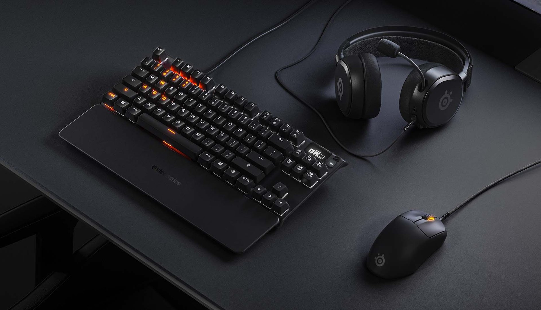 Schwarze Tastatur, Maus und Headset auf einem Schreibtisch. Orangefarbene Tasten und Beleuchtung vorhanden.