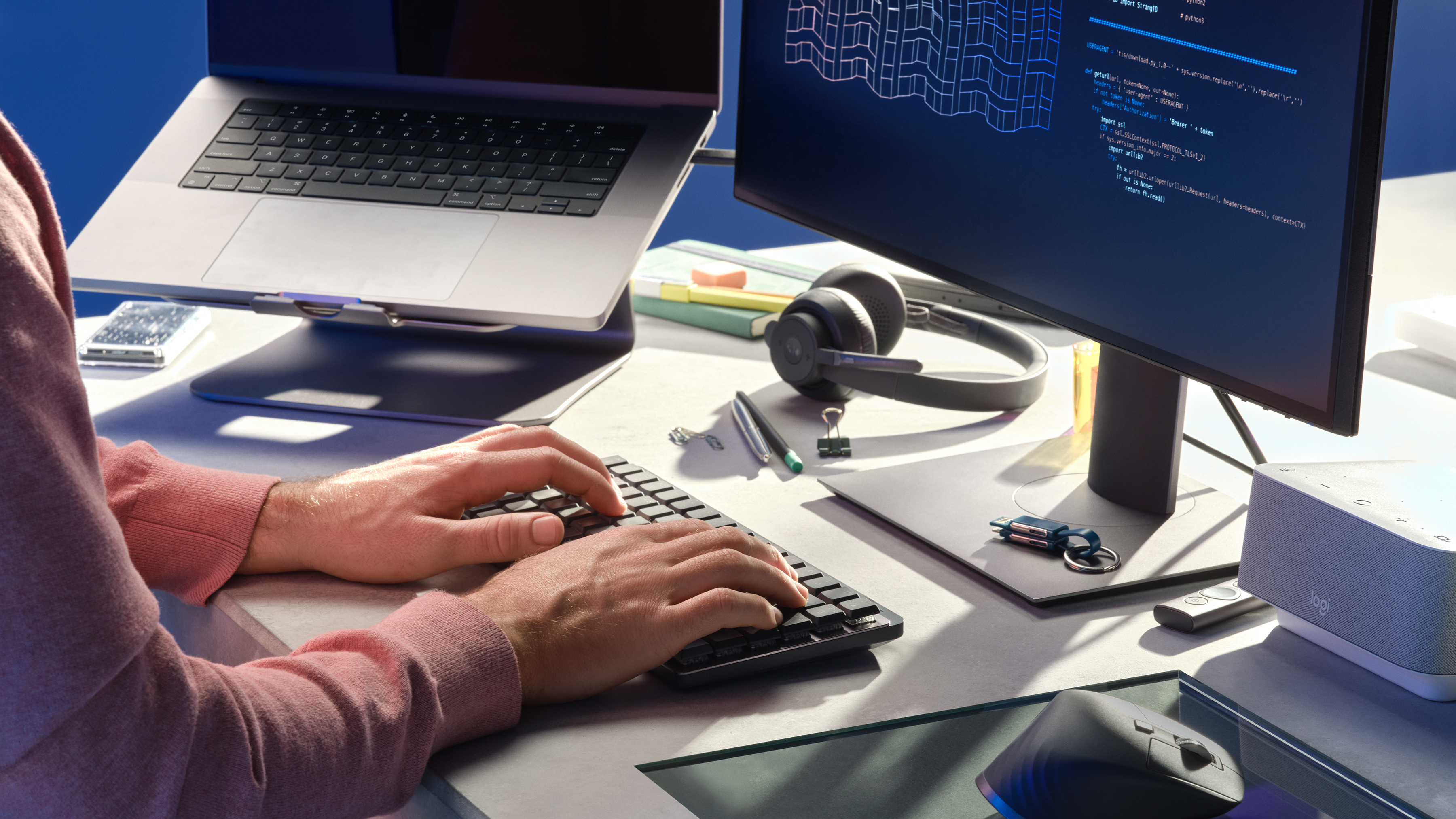 Eine Person tippt auf einer schwarzen Tastatur, mit Laptop, Monitor und Maus.