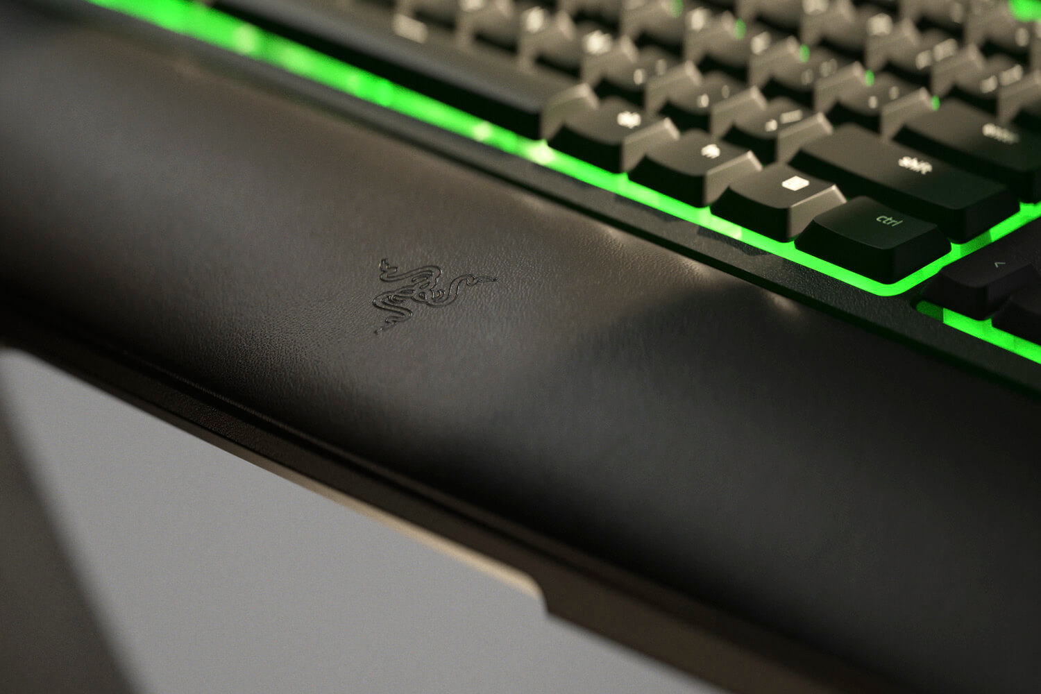 Nahaufnahme einer schwarzen Tastatur mit Razer-Logo und grüner Hintergrundbeleuchtung.