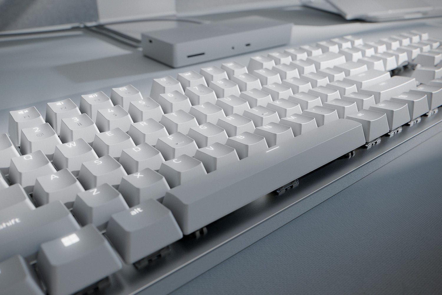 Gros plan sur un clavier blanc sur une surface gris clair. Un petit appareil gris en arrière-plan.