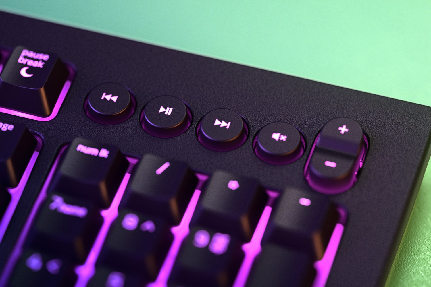 Nahaufnahme einer Tastatur mit Medientasten und lila/rosa Beleuchtung auf grüner Oberfläche.