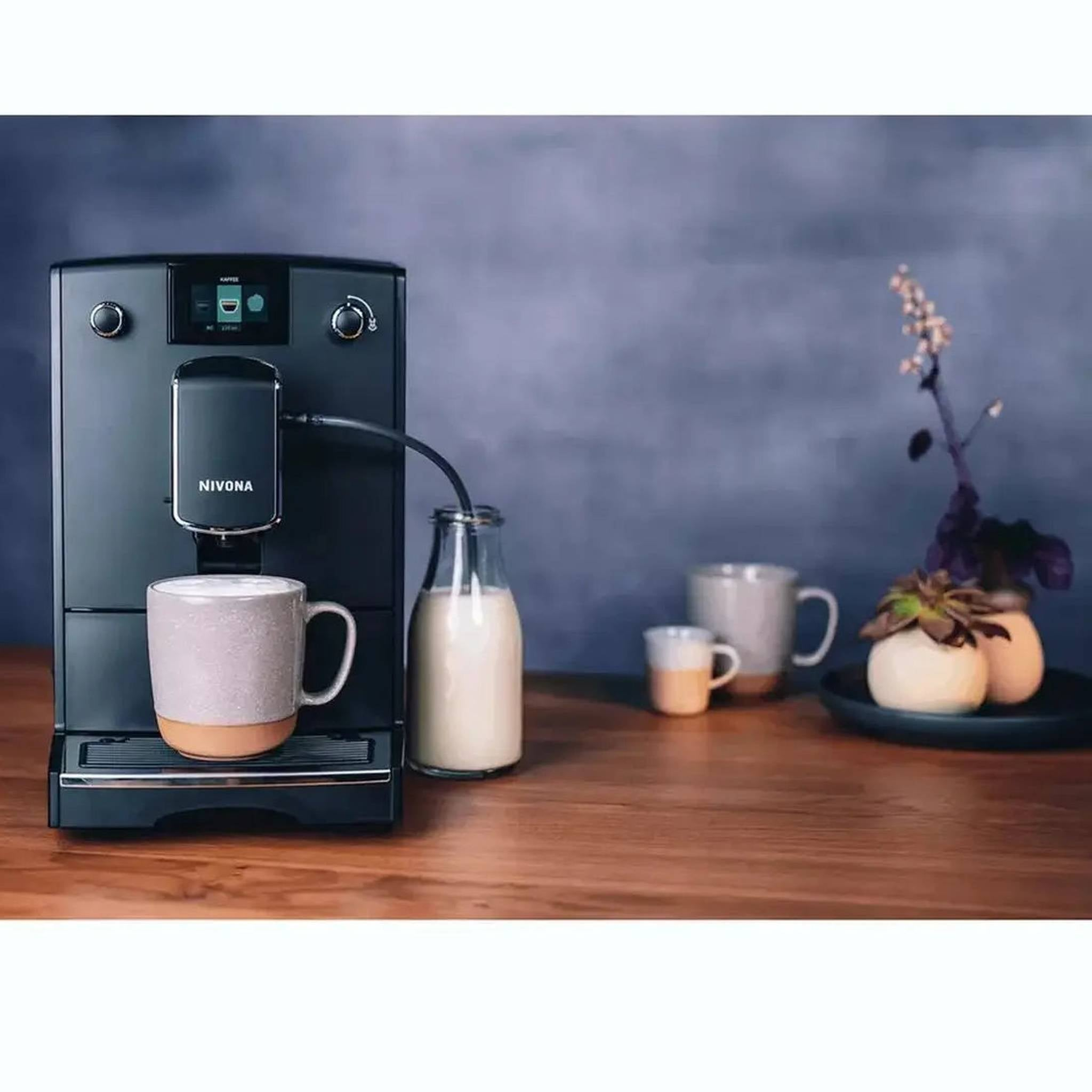 Macchina da caffè nera con tazza, caraffa di latte e due tazze su un tavolo di legno.