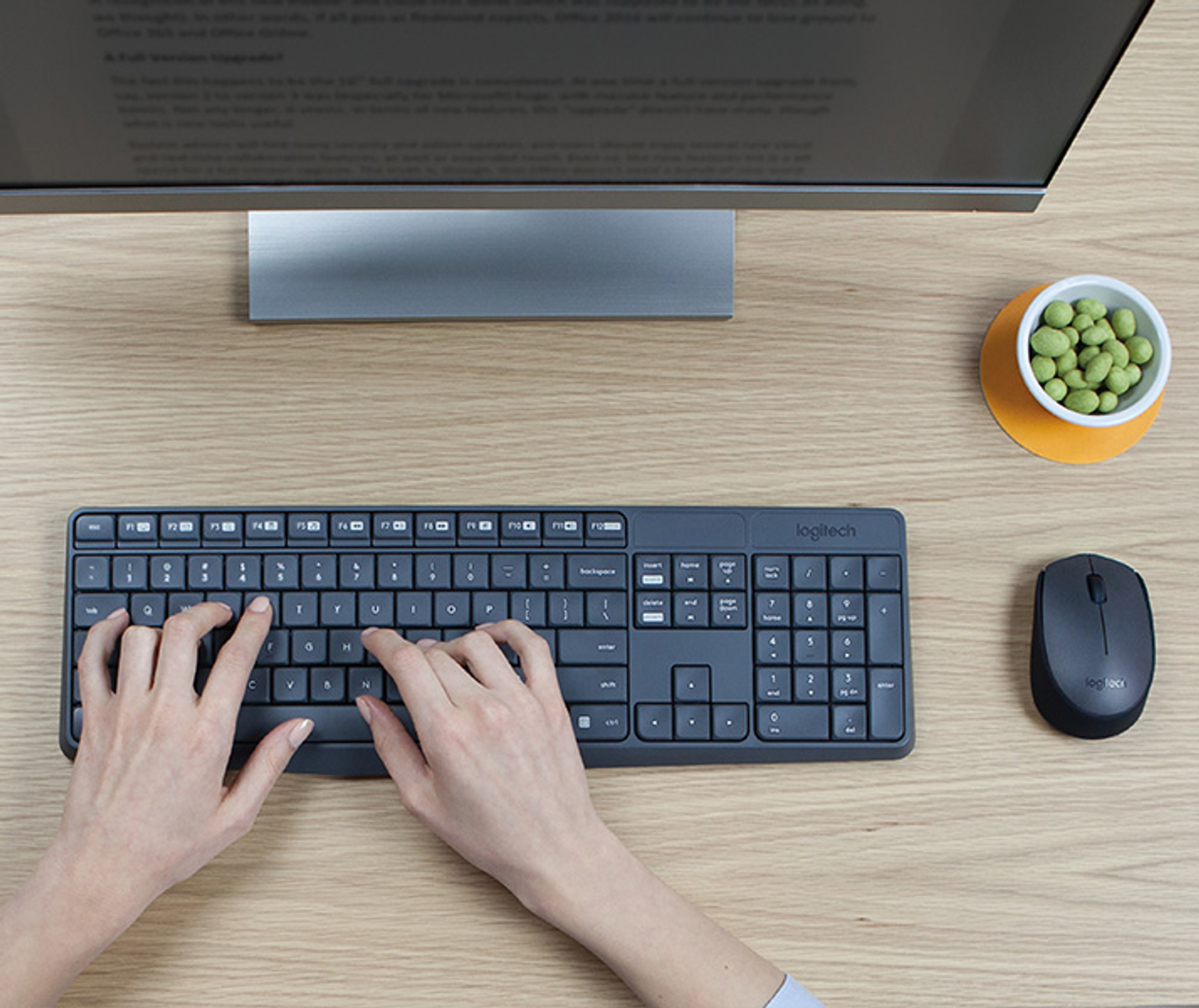 Mani che digitano su una tastiera Logitech, con mouse e ciotola di snack nelle vicinanze.