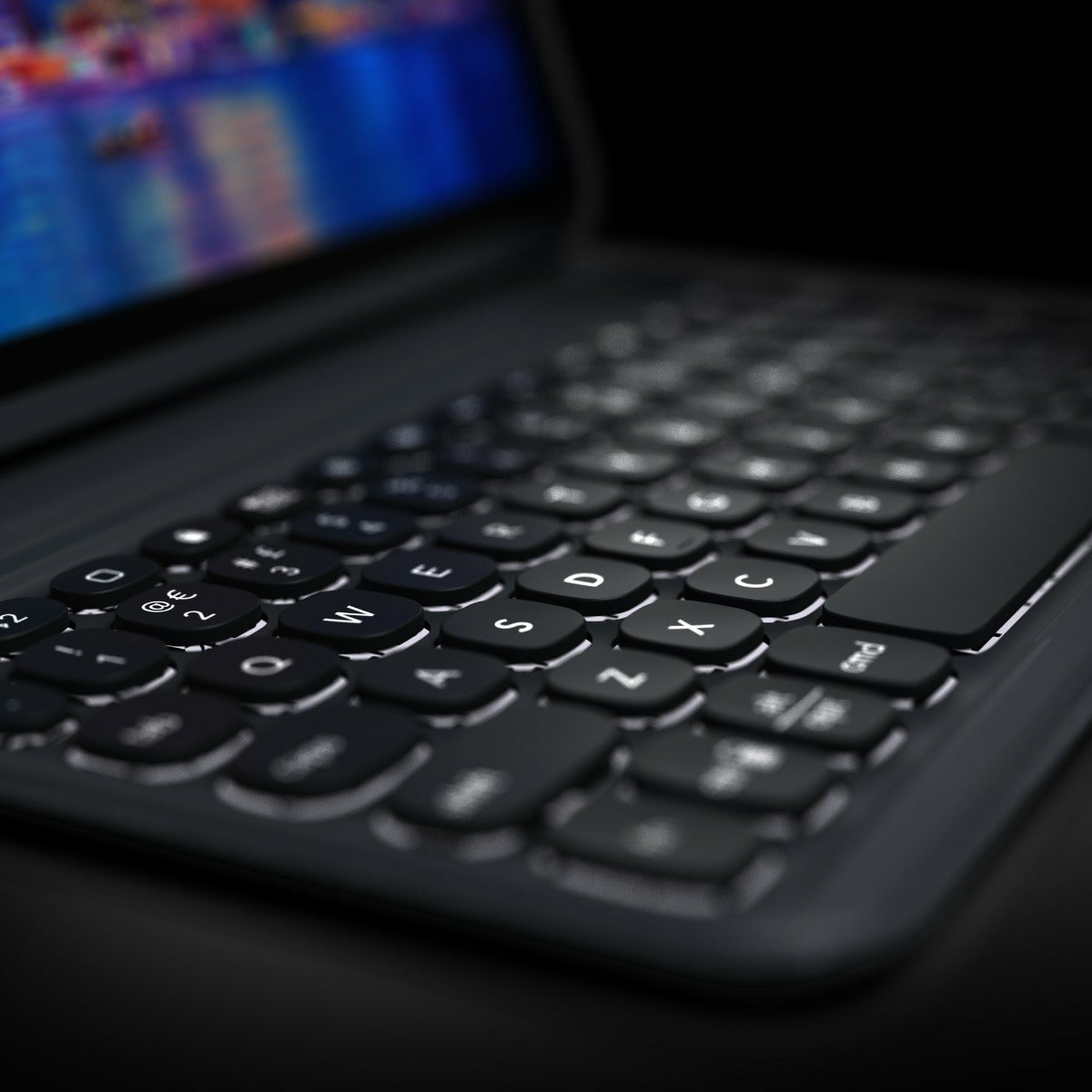Close-up of a black keyboard on a laptop. White letters and symbols on keys. Blurred screen background.