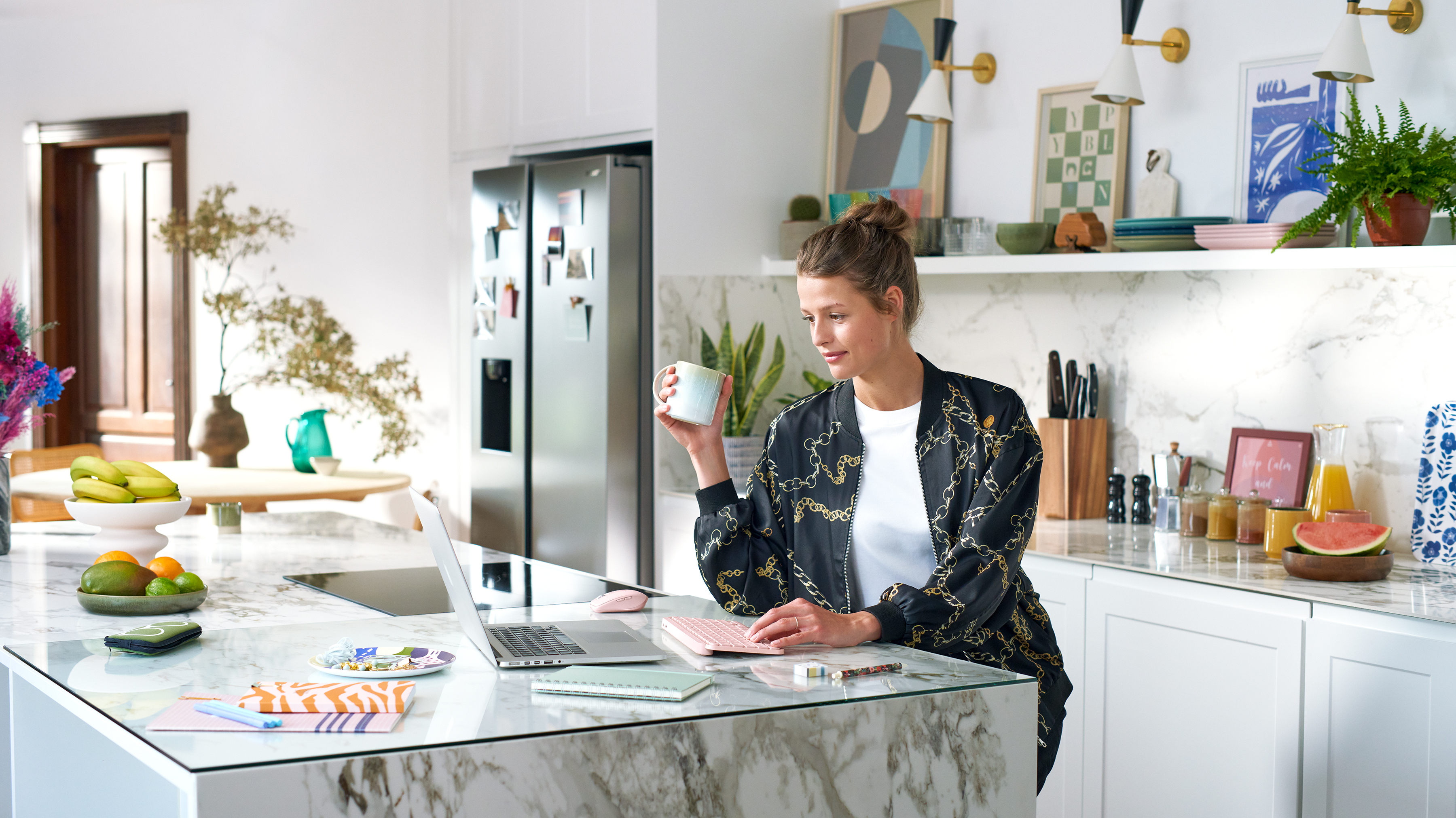 Kobieta w kuchni z laptopem, trzymająca kubek. Wyspa kuchenna, białe szafki.