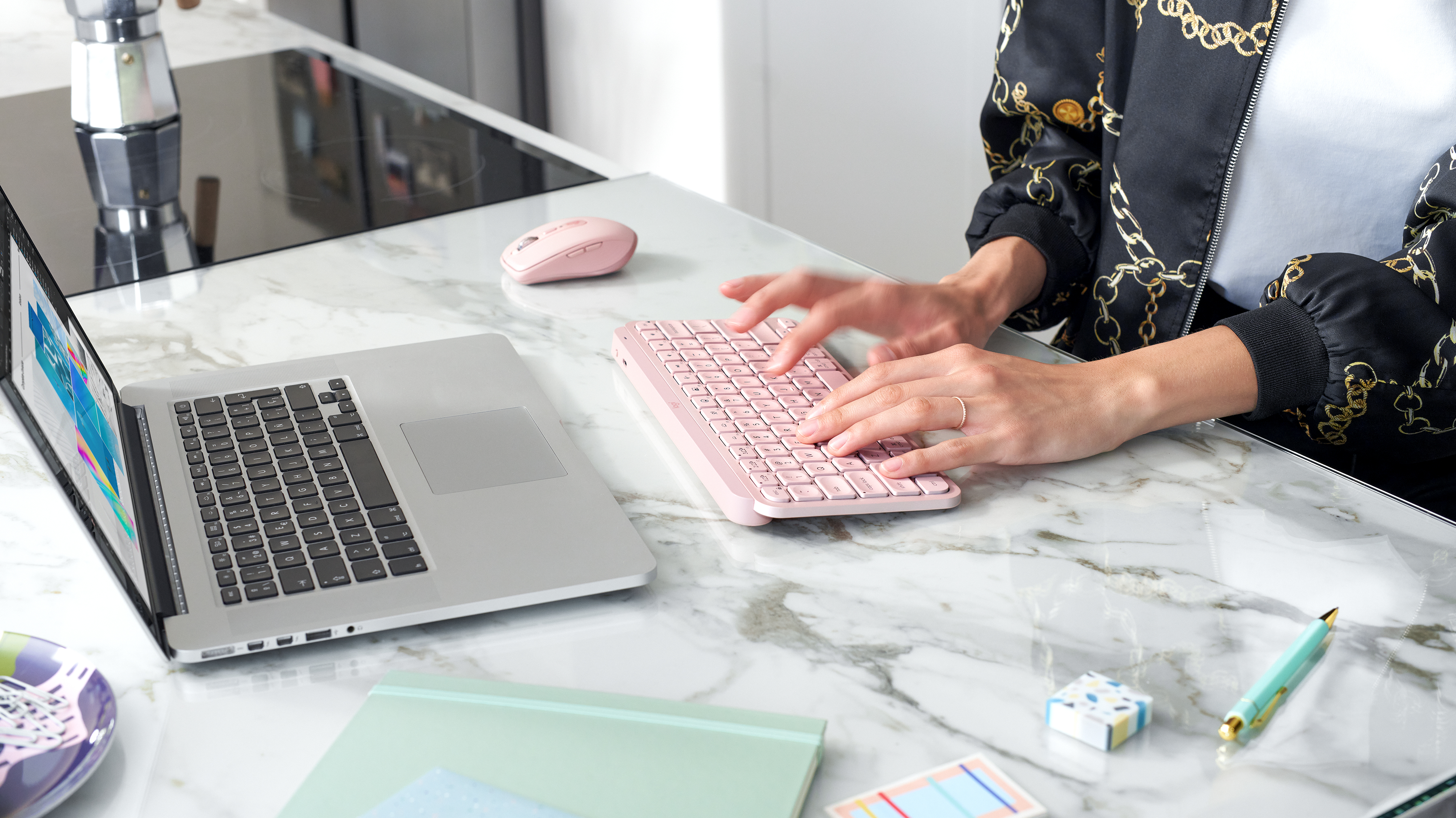 Osoba pisząca na różowej klawiaturze i używająca różowej myszy. Otwarty laptop i inne przedmioty.