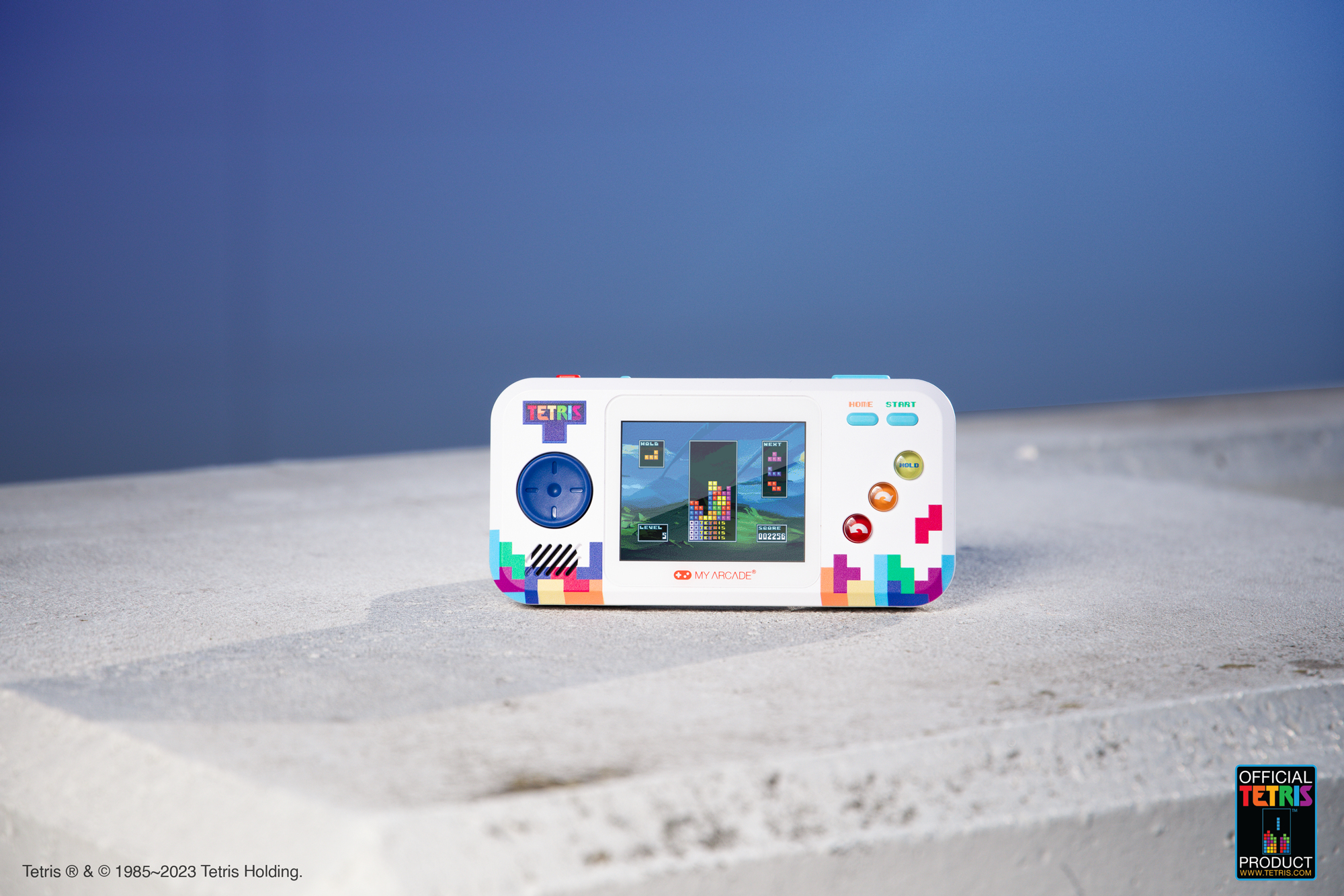 Biała przenośna gra Tetris z kolorowymi przyciskami, ekranem z rozgrywką, na jasnej powierzchni.