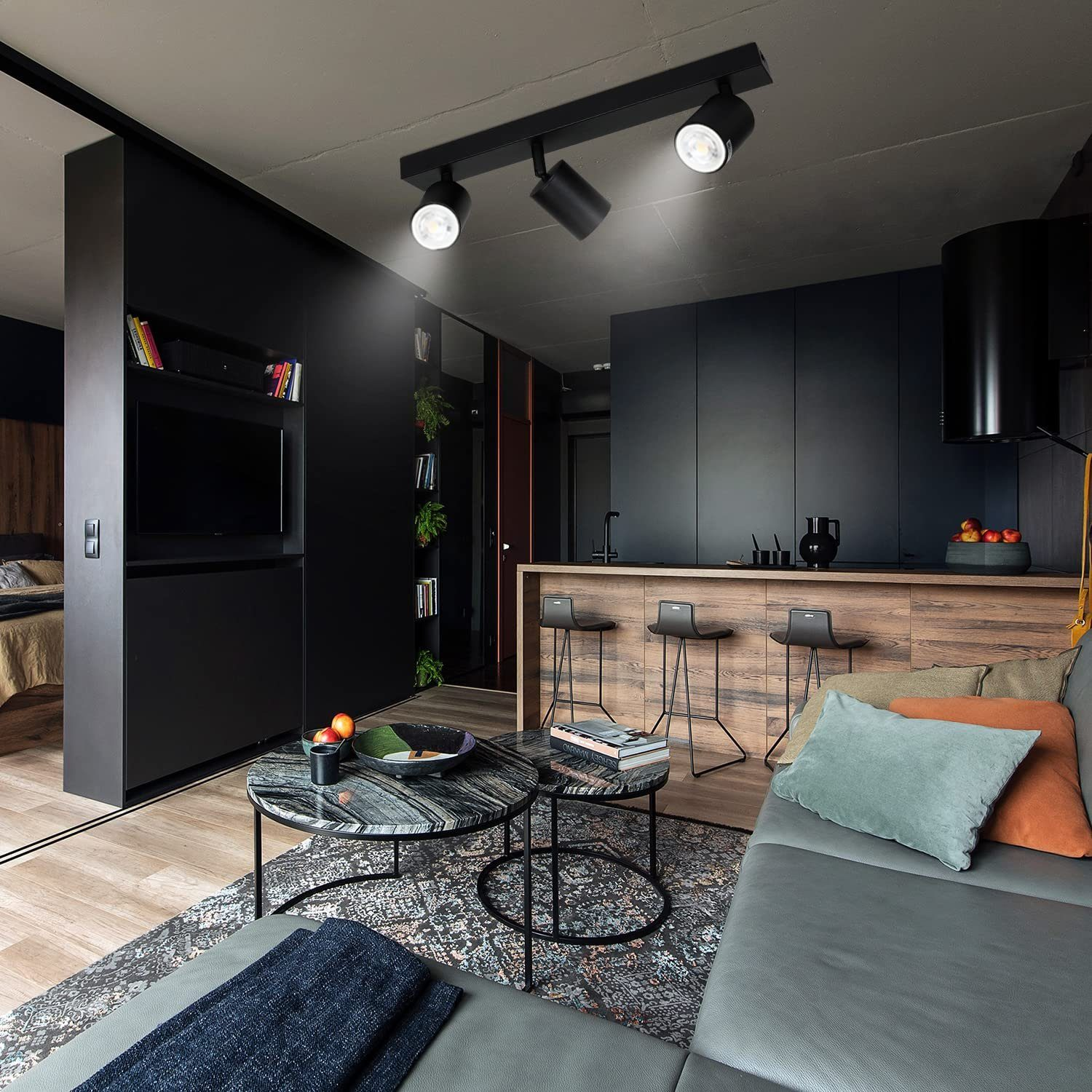 Nowoczesny salon z trzema reflektorami, szarą sofą i aneksem kuchennym.