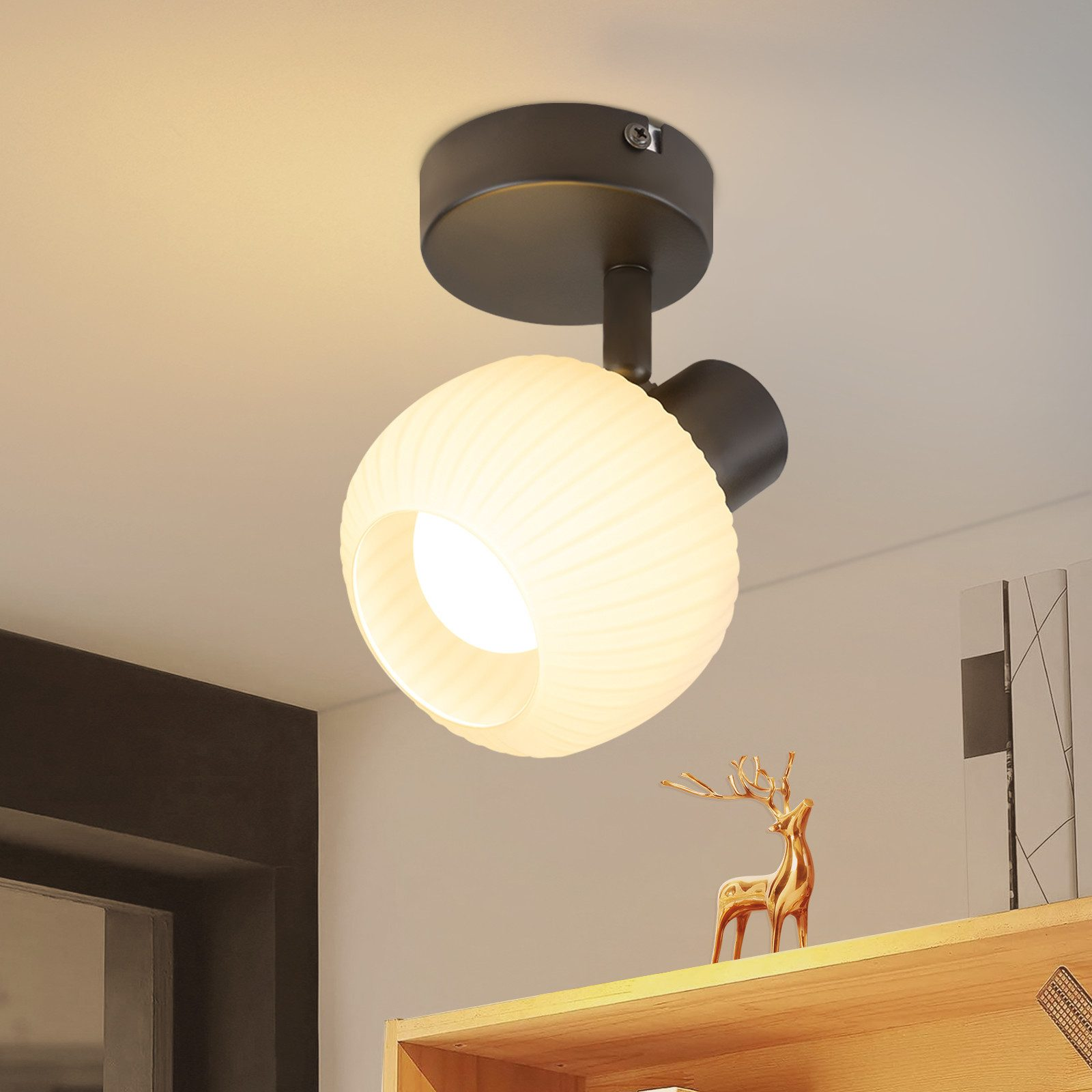 Okrągła biało-czarna lampa sufitowa. Złoty renifer i drewniana półka w tle.
