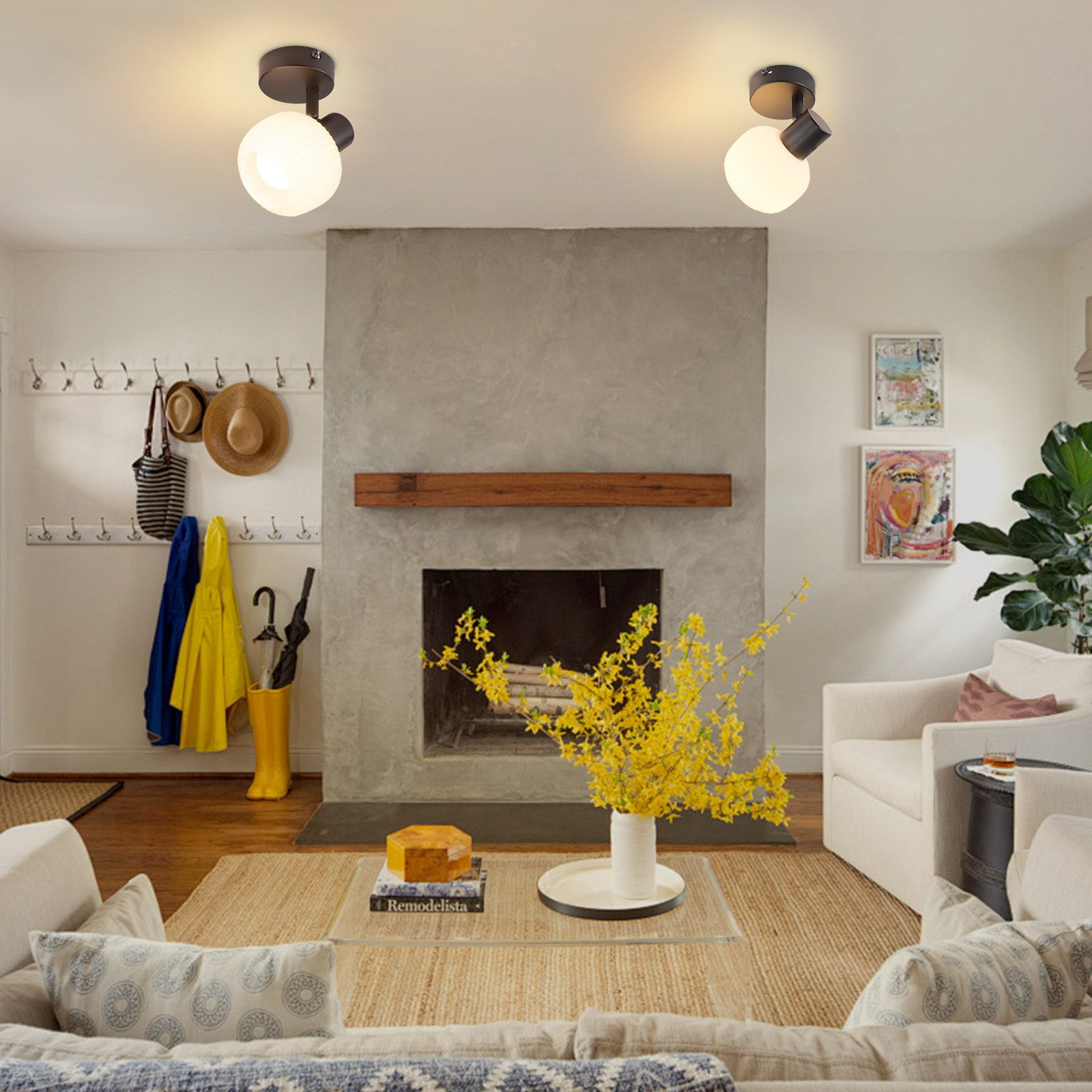 Salon z kominkiem, kwiatami i dwoma lampami sufitowymi. Białe ściany i meble.