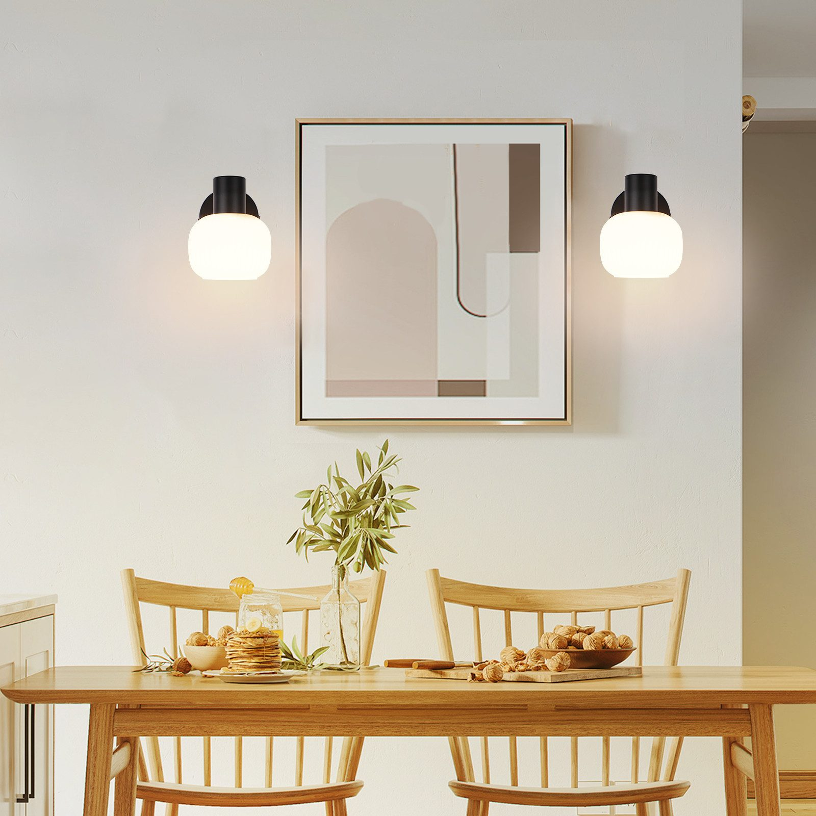 Dwie lampy ścienne z białymi szklanymi kloszami flankują oprawione abstrakcyjne dzieło sztuki nad stołem.