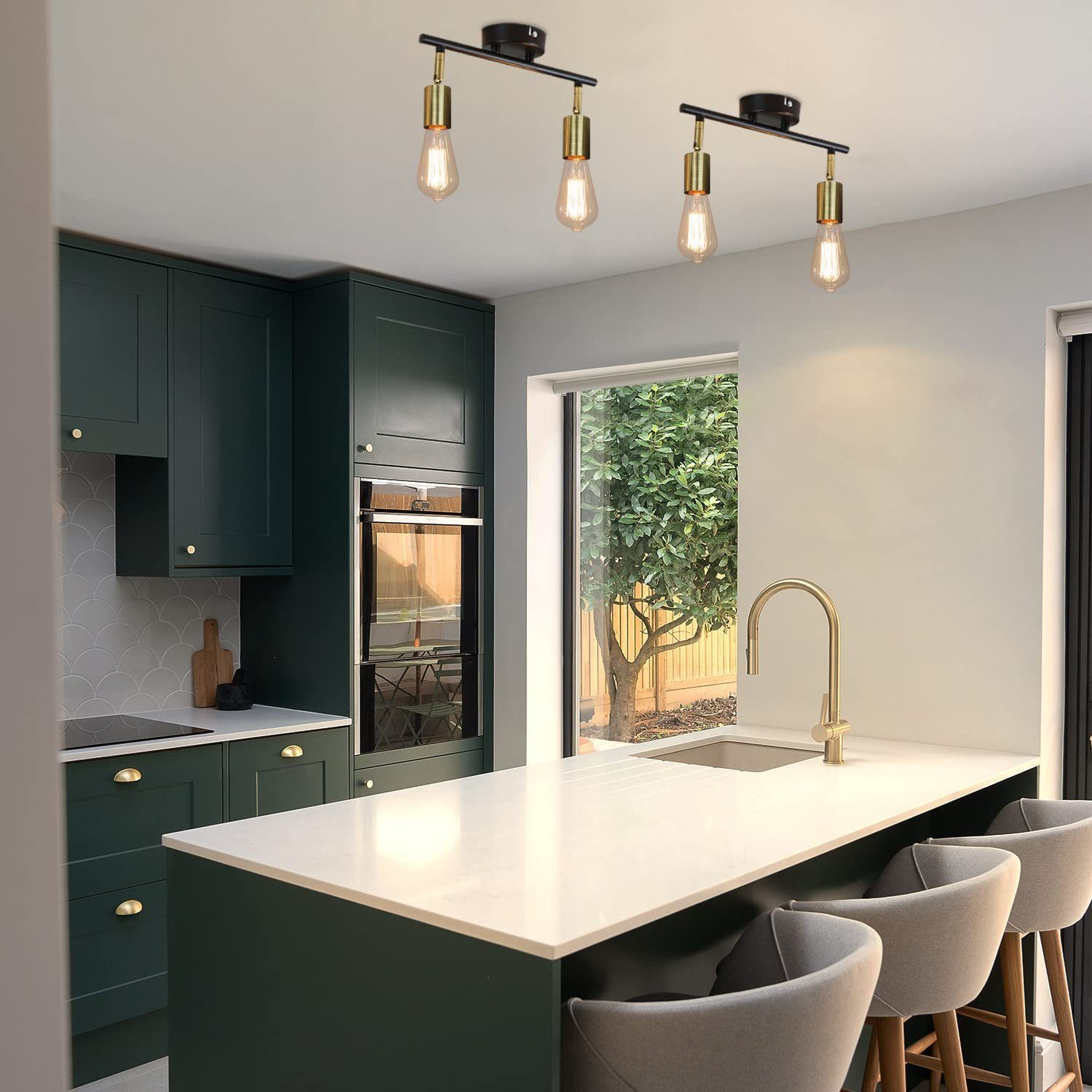 Nowoczesna kuchnia z zielonymi szafkami, białymi blatami i wiszącymi lampami. Okno ukazuje drzewo na zewnątrz.