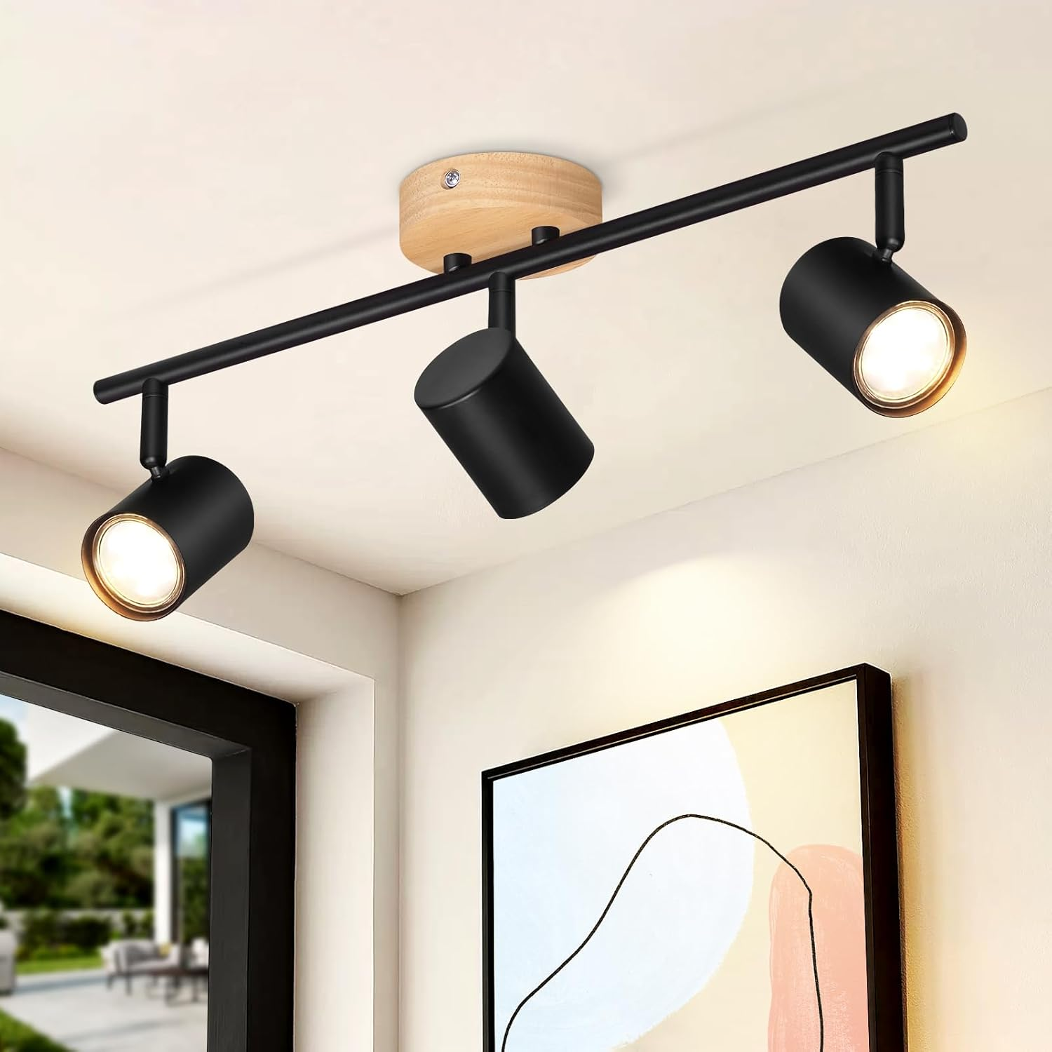 Czarny reflektor sufitowy z 3 regulowanymi głowicami, zamontowany na drewnianej podstawie. Tło: jasna ściana i obraz.
