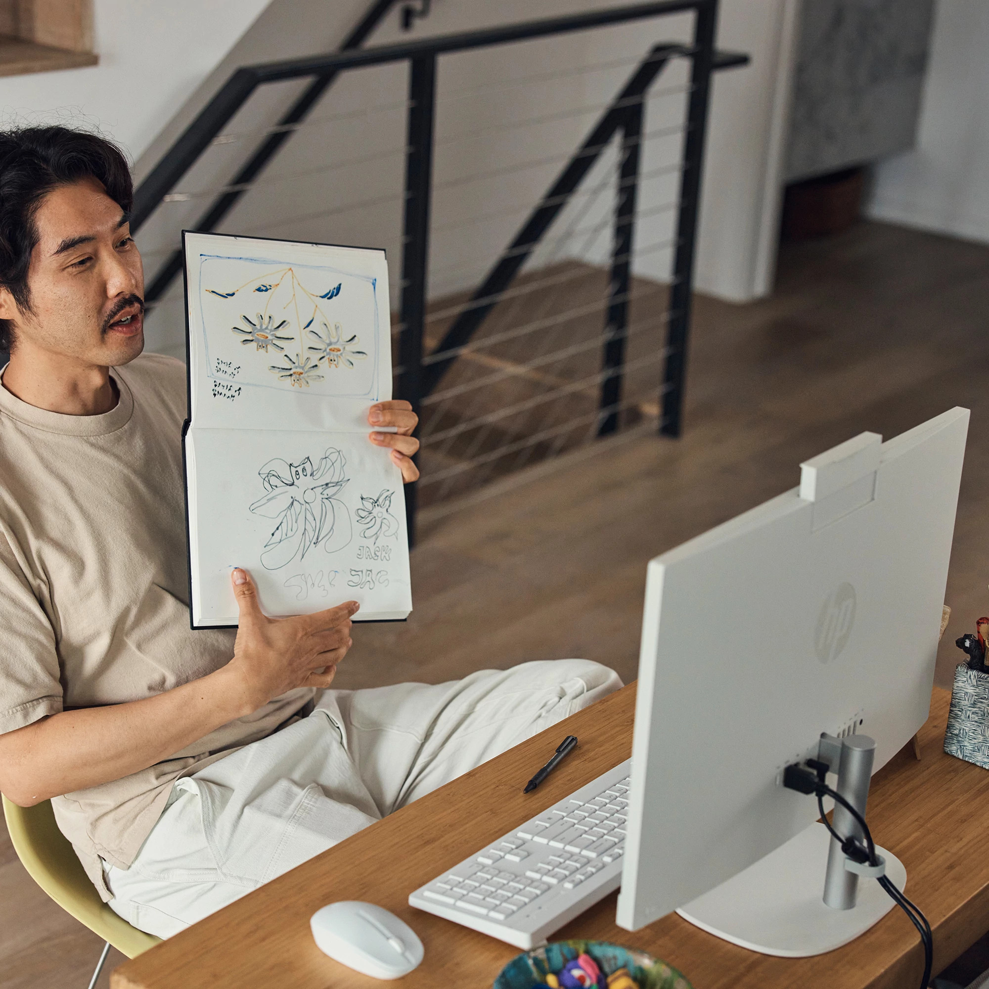 Mężczyzna prezentujący rysunki w notatniku podczas rozmowy wideo na białym komputerze all-in-one.