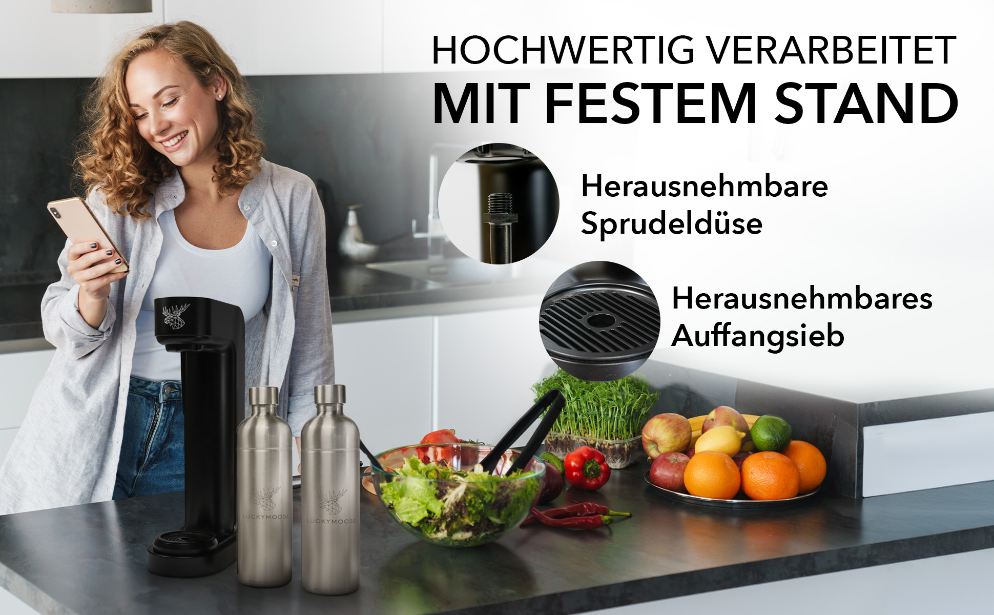 Eine Frau mit Telefon lächelt in einer Küche. Flaschen, Salat und Wasserspender stehen auf der Theke.